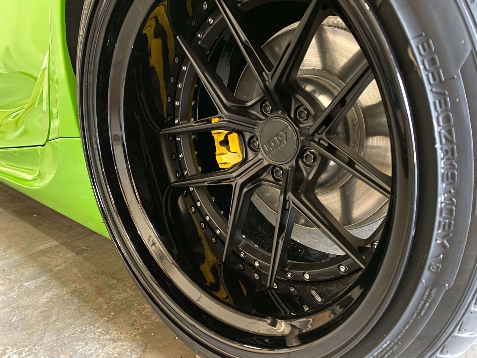 Close-up of a lime green car’s black alloy wheel with a yellow brake caliper.