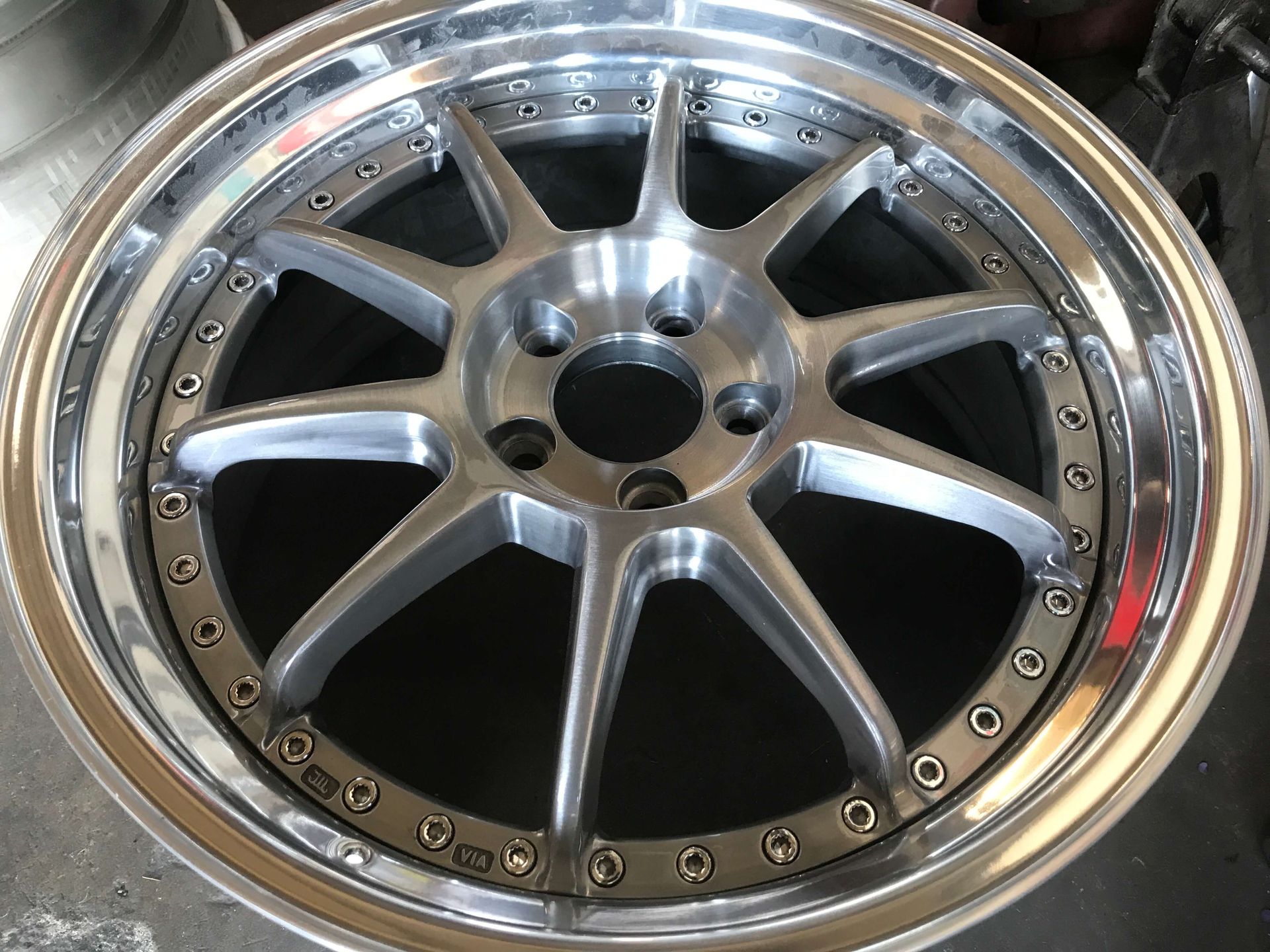 Close-up of a silver multi-spoke car wheel rim with rivets around the outer edge