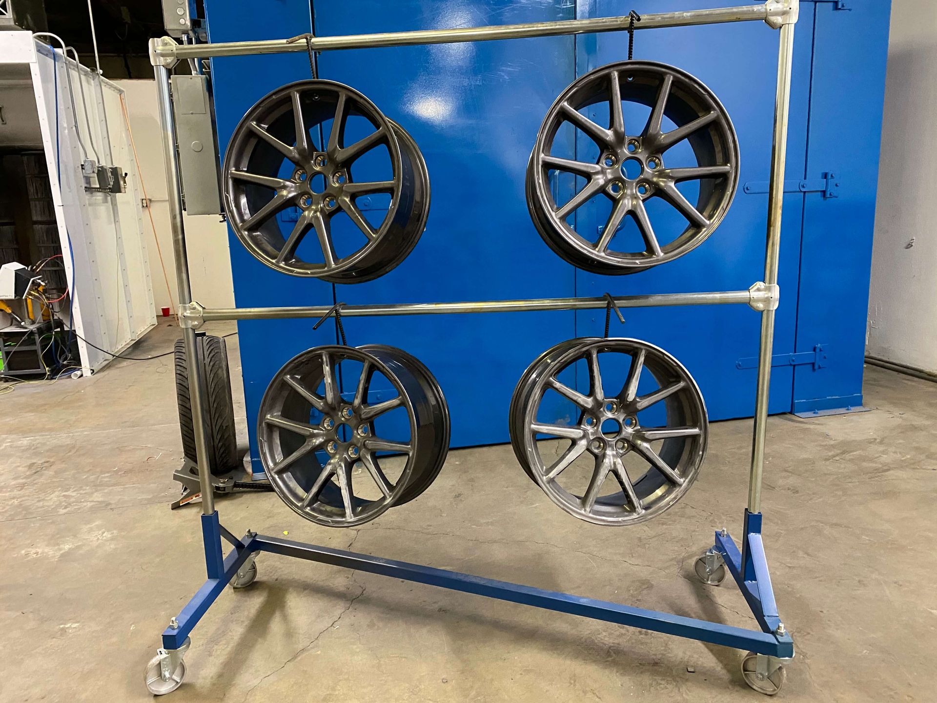 Four alloy car wheels mounted on a metal display rack in a workshop.