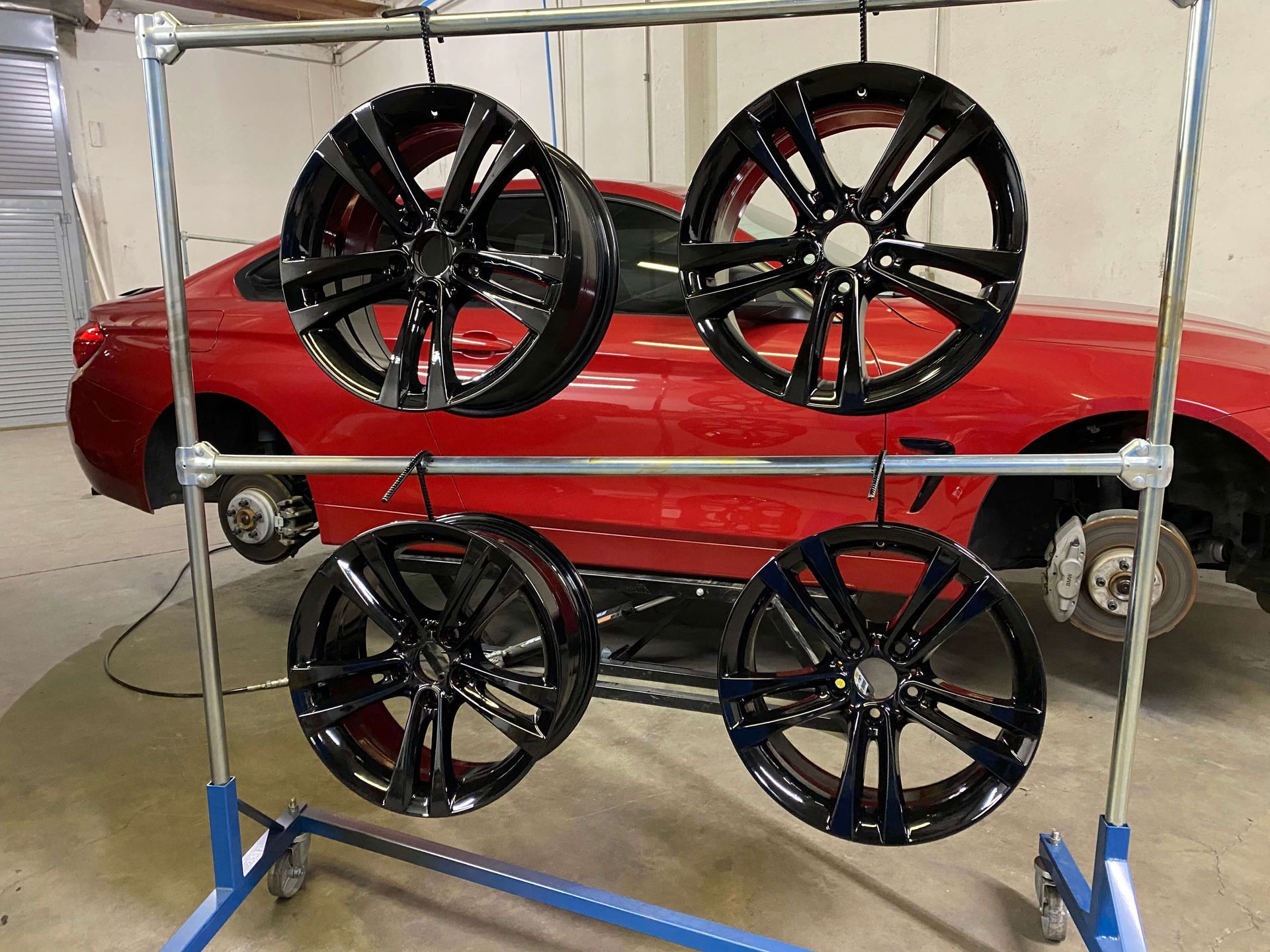 Red sports car behind a rack of four glossy black alloy wheels in a showroom-like setting