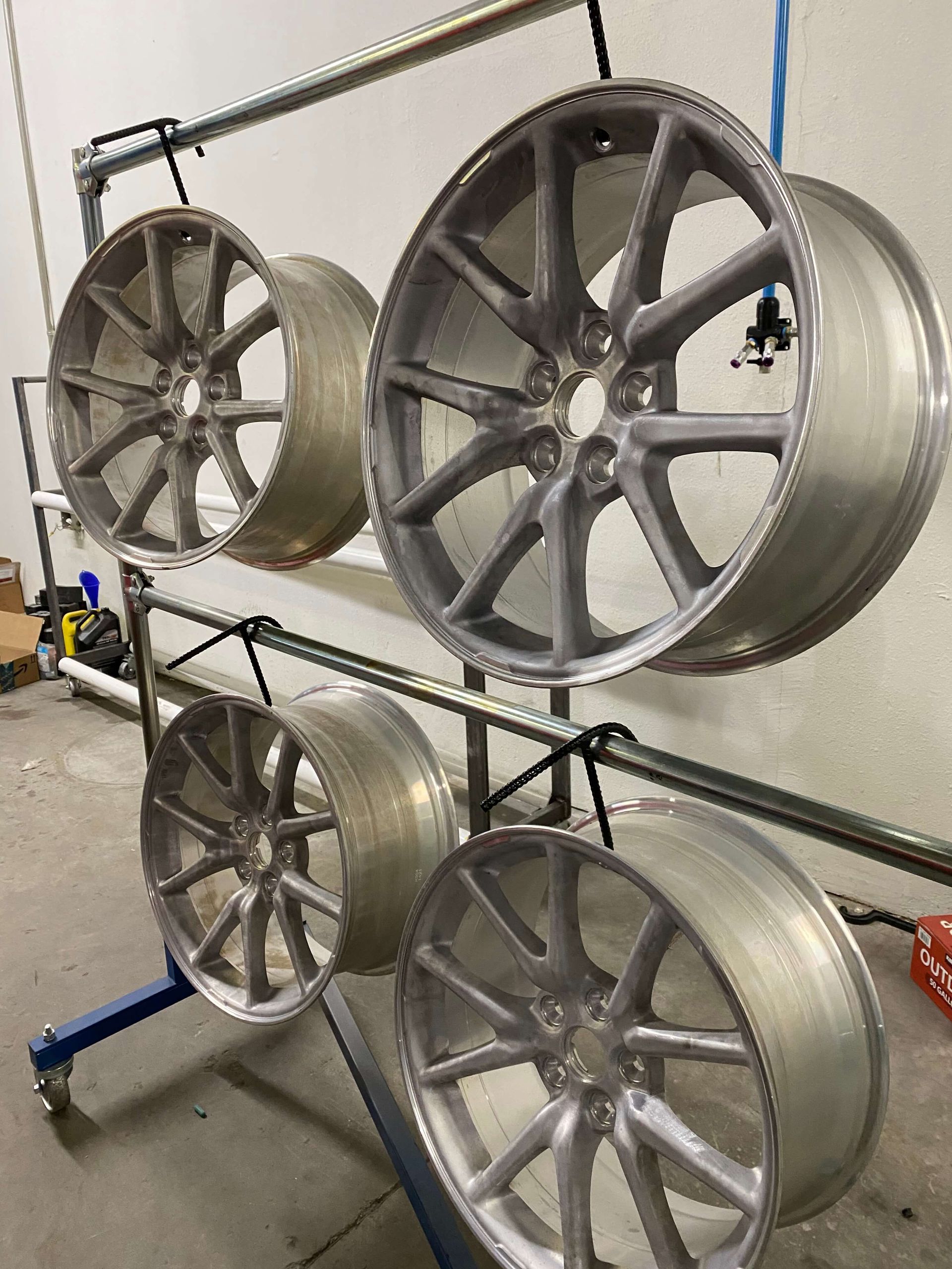Four silver alloy wheels mounted on a display rack in a workshop.