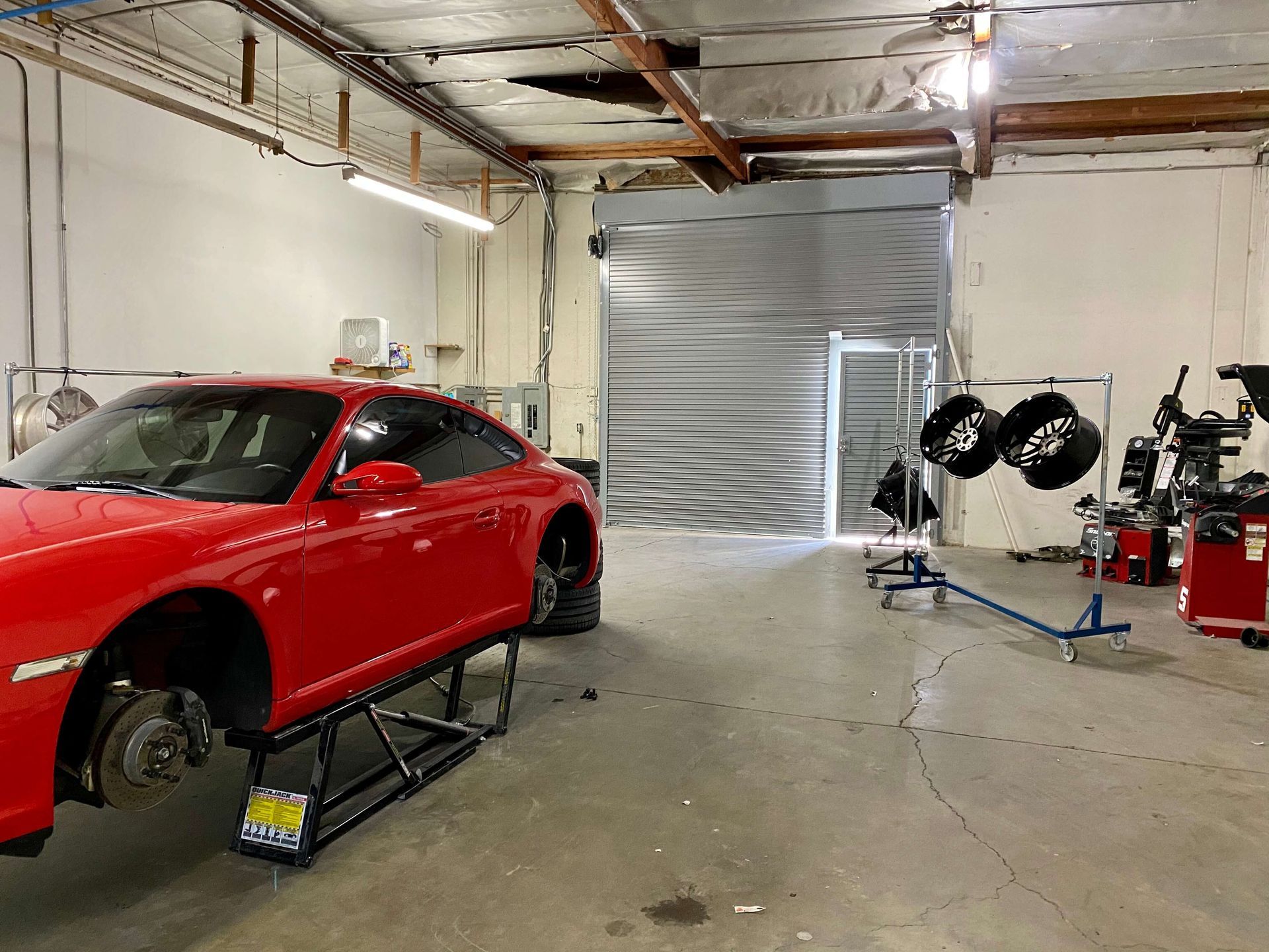 Red sports car in a workshop garage with a wheel removed and equipment in the background