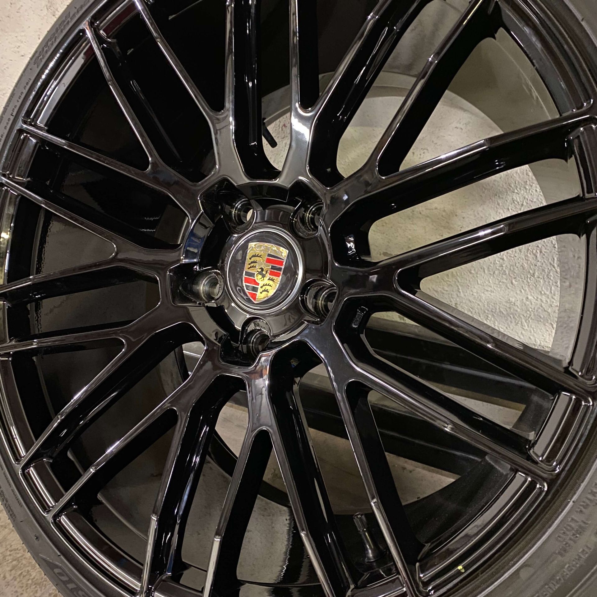 Glossy black Porsche alloy wheel with multi-spoke design and crest center cap
