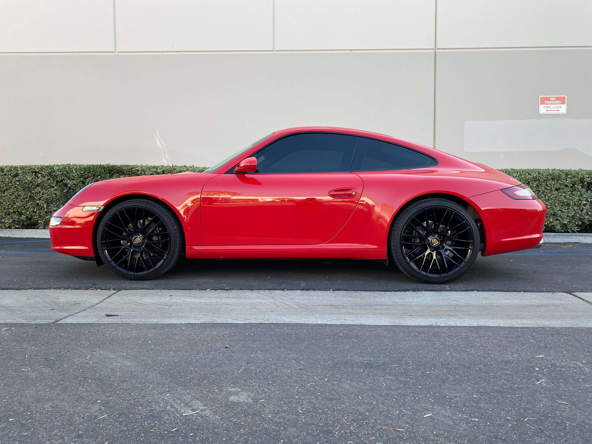 Red sports coupe parked beside a hedge and gray wall