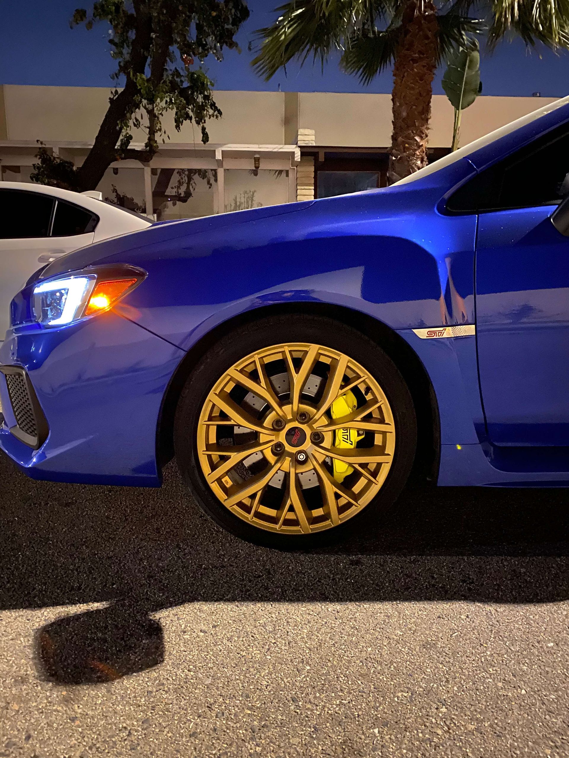 Blue sports car with gold rims parked at night on a street
