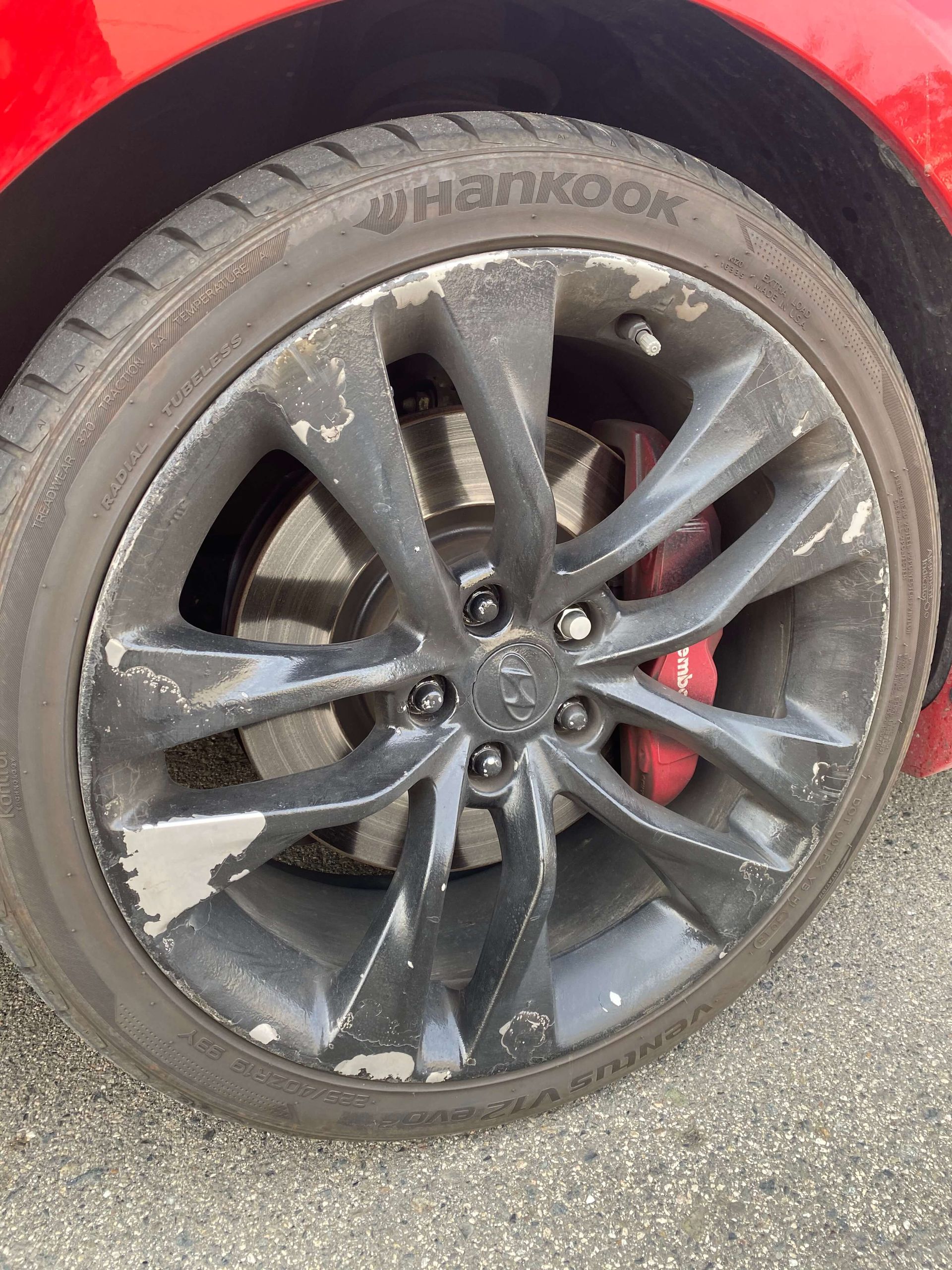 Dirty black car wheel with a multi-spoke rim and visible red brake caliper, close-up on pavement