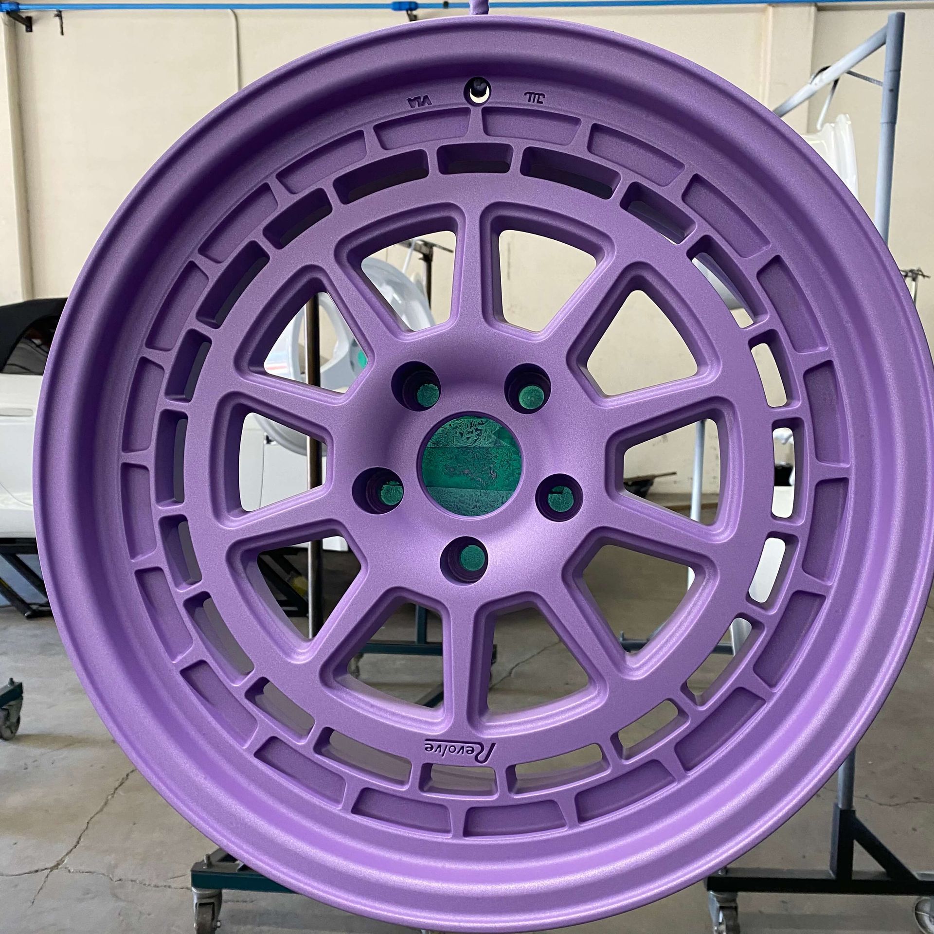 Purple alloy car wheel rim with turquoise center hub, photographed front-on.
