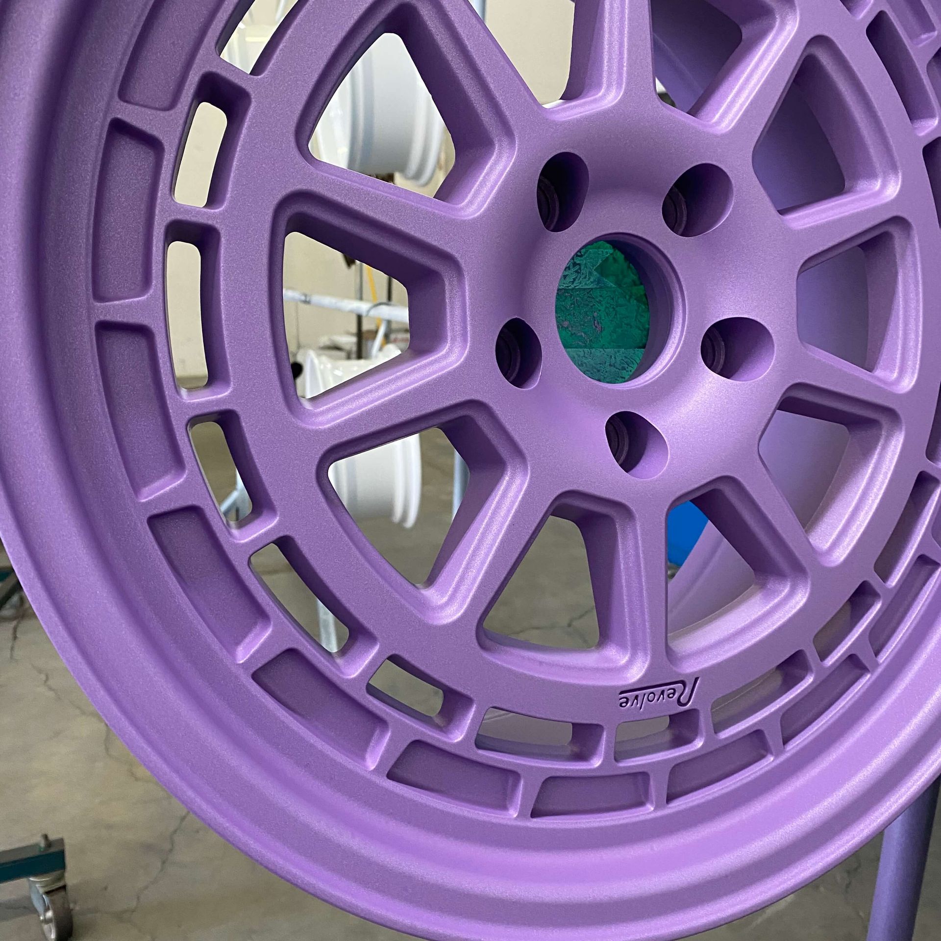 Purple alloy car wheel rim with multi-spoke design, shown close-up in a garage.