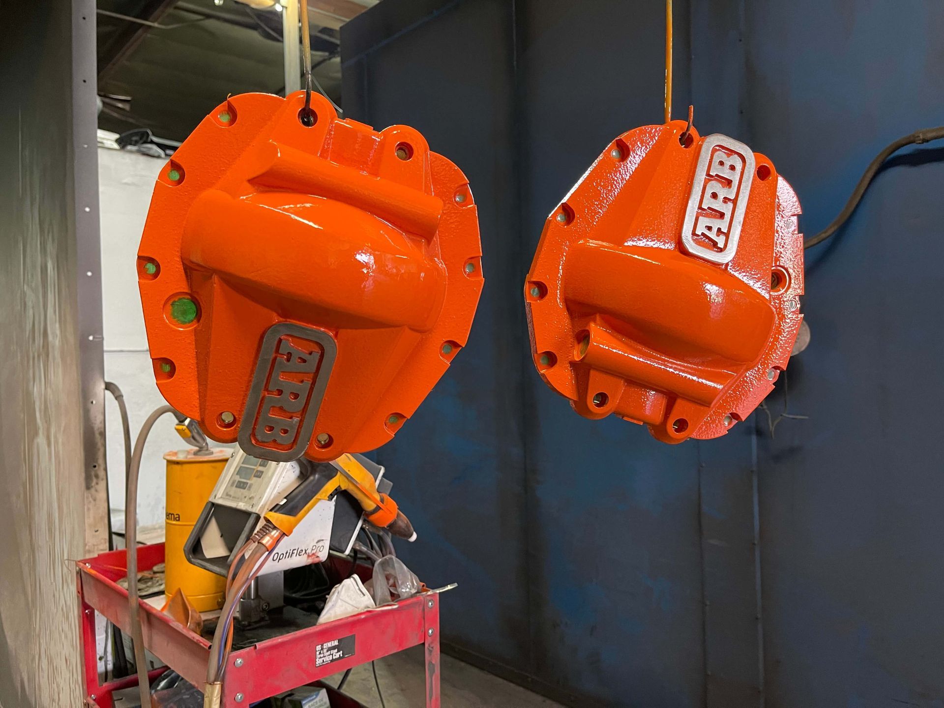 Two orange industrial valves hanging in a workshop, one over a red cart with tools.