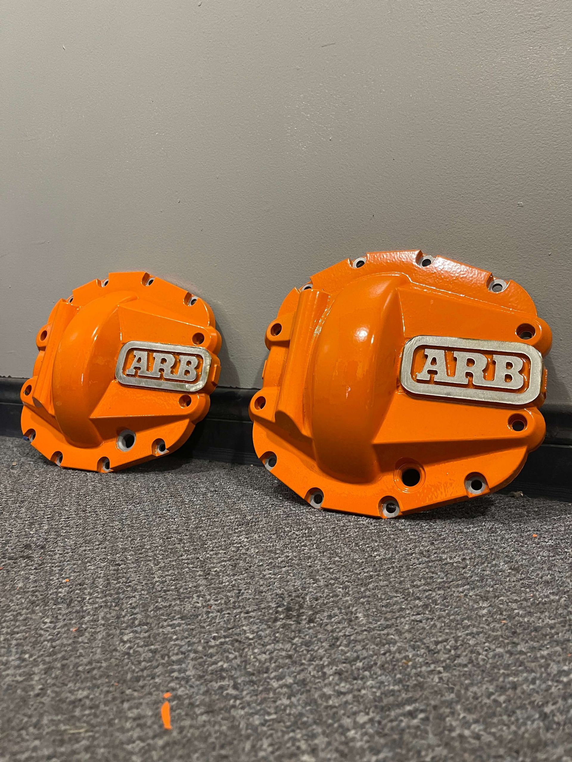 Two orange ABB industrial robot heads on a gray carpet, one larger than the other.