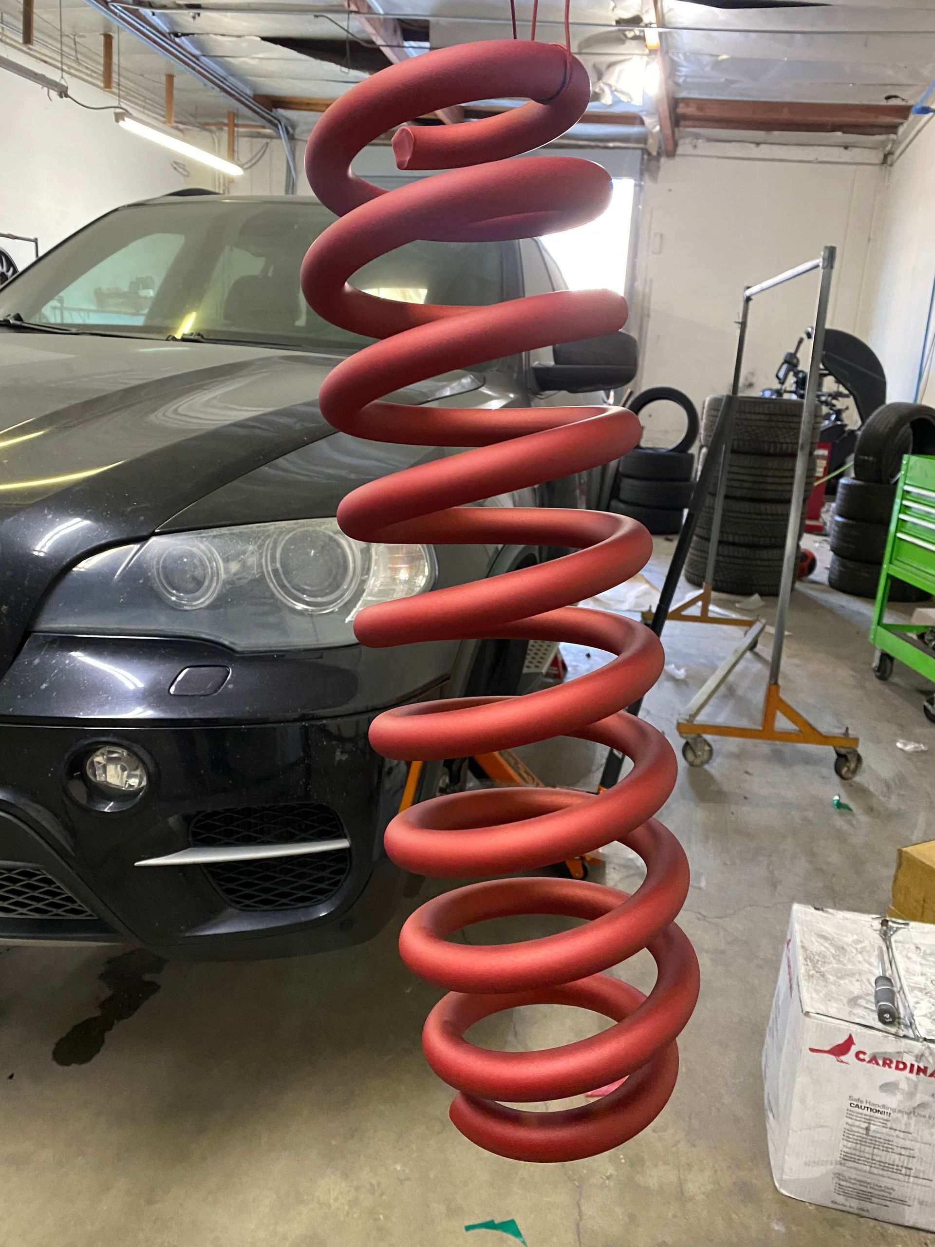 Red coil spring hanging in a garage in front of a black car