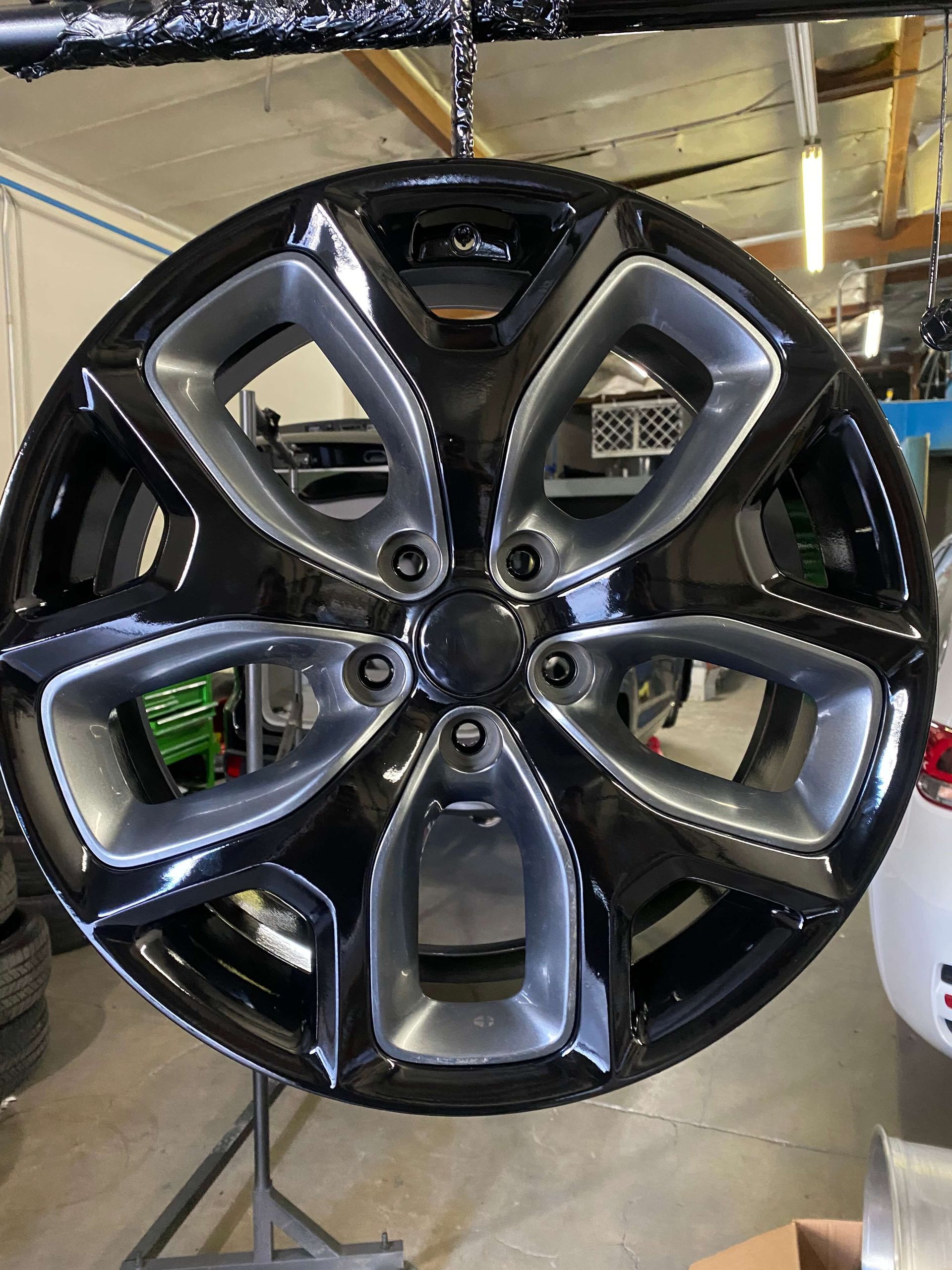 Glossy black alloy wheel rim with six spokes, hanging in a garage or workshop.