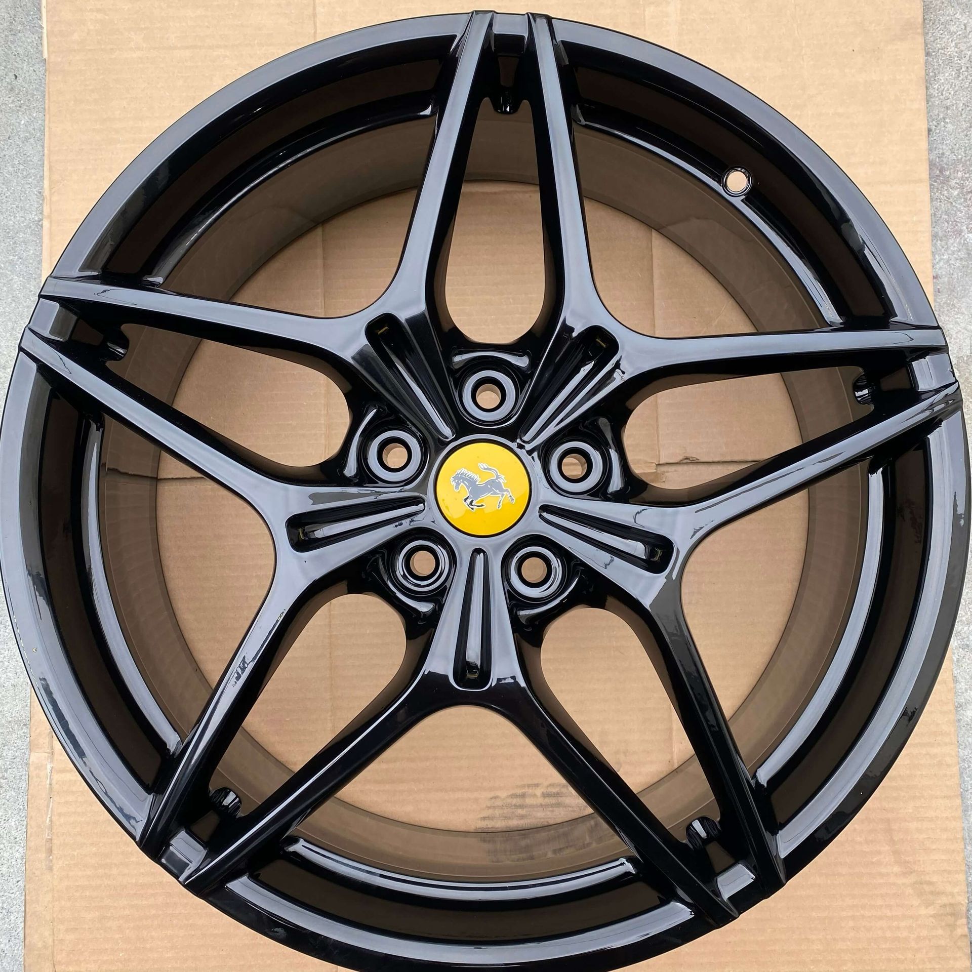 Black multi-spoke car wheel rim with a yellow center logo on cardboard packaging