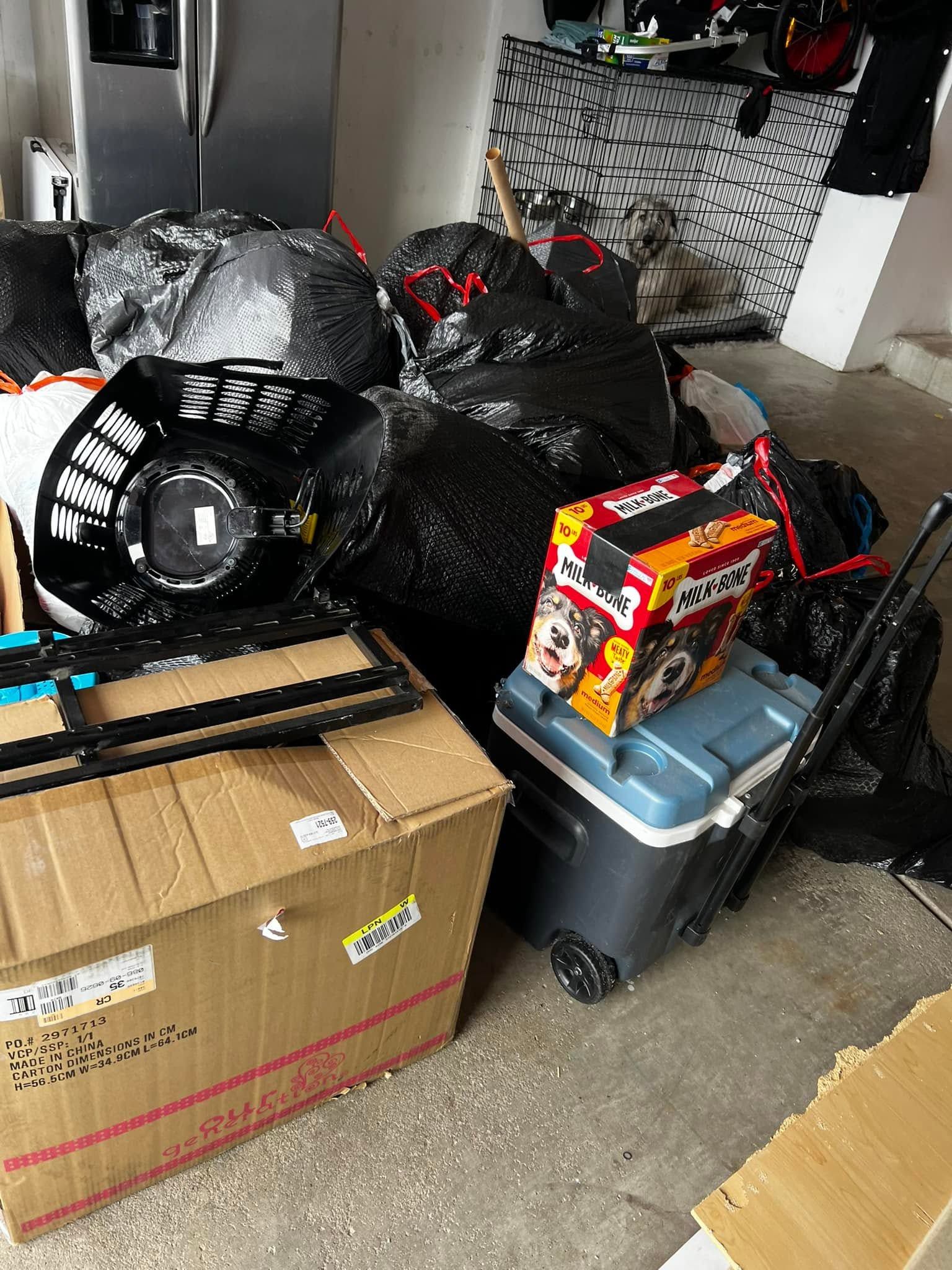 Garage cluttered with black trash bags, a cardboard box, and a gray storage bin with a red toy box on top