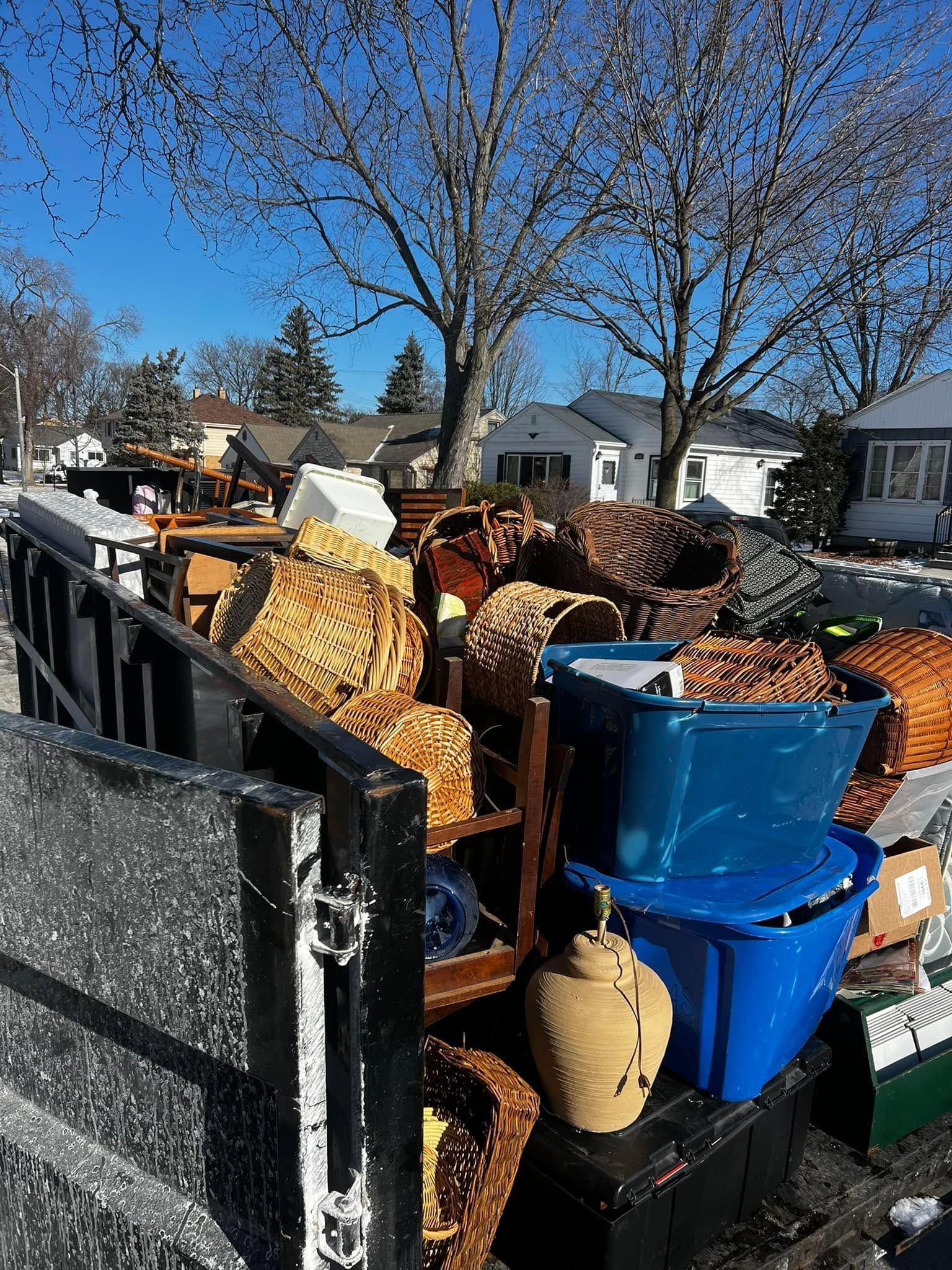 Overflowing trash bin full of wicker furniture and blue plastic bins on a sunny residential street