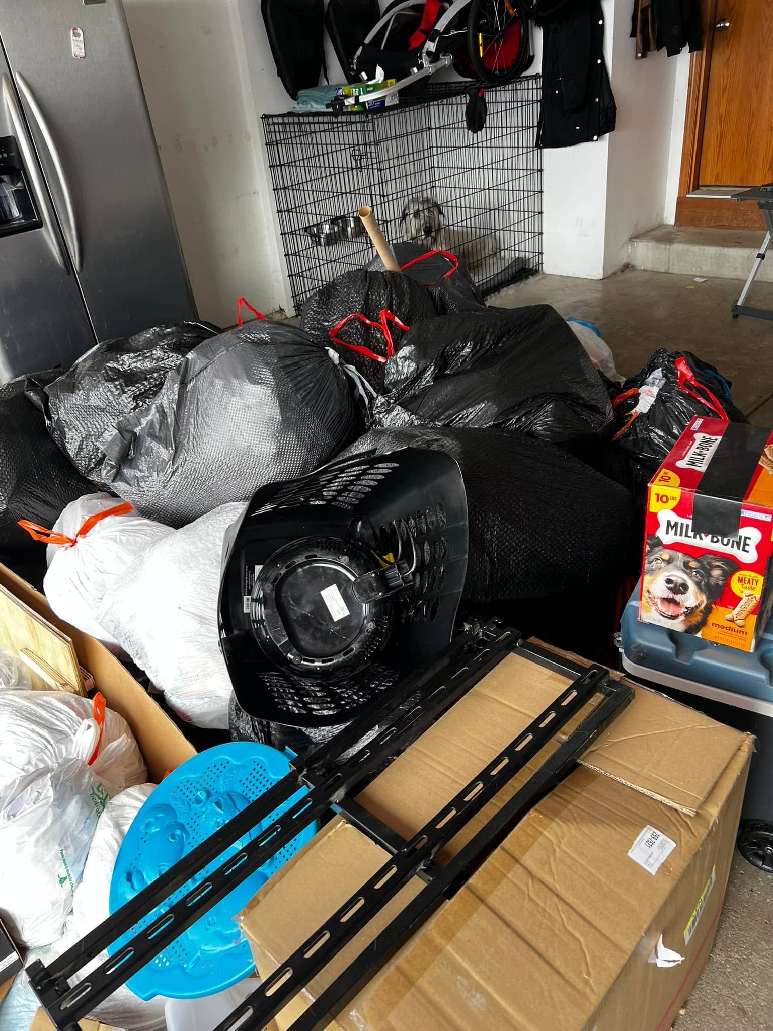 Piles of black trash bags and cardboard boxes clutter a garage floor near a fireplace.