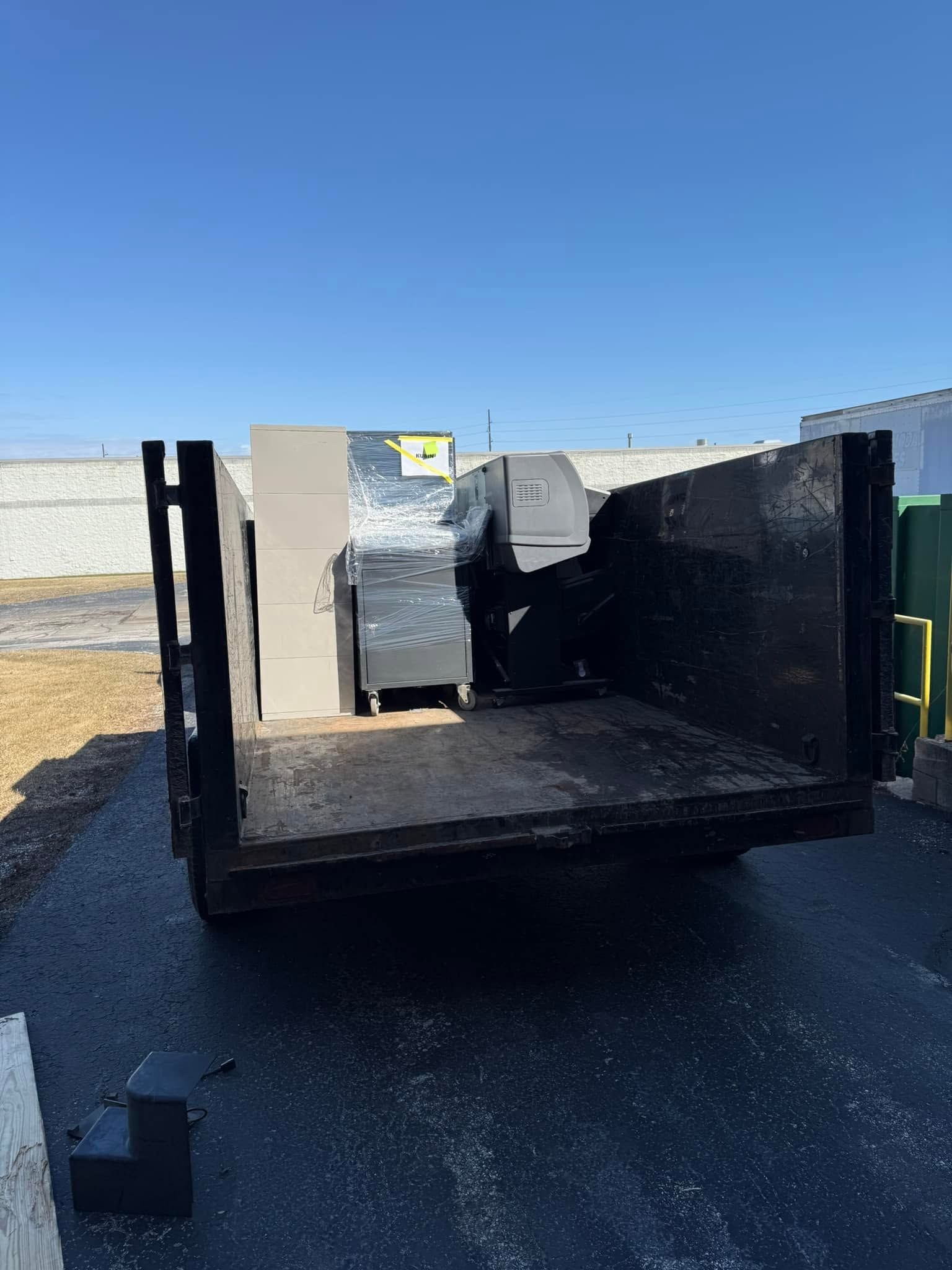 Black metal dumpster bin in an outdoor lot under a clear blue sky.