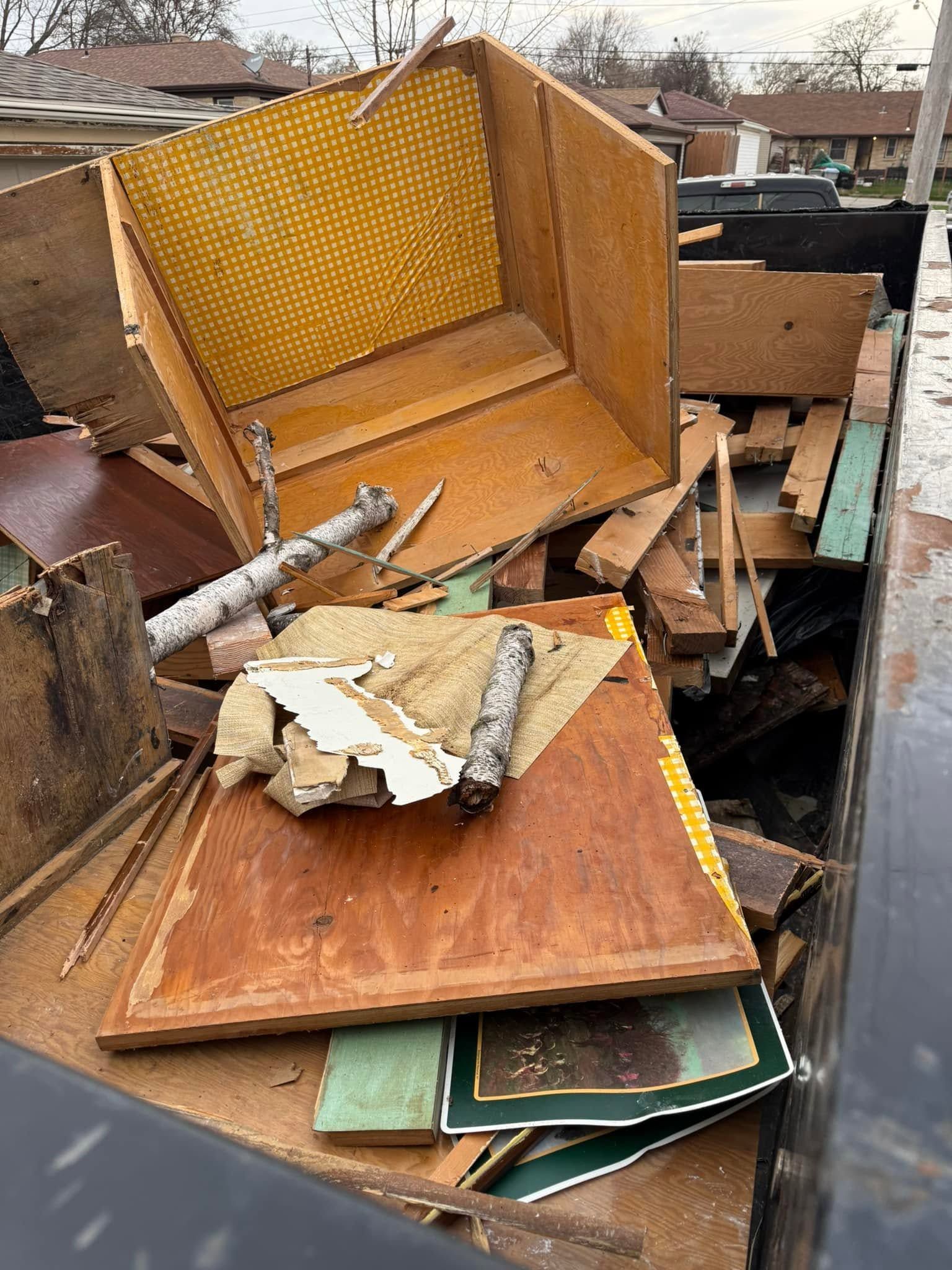 Pile of discarded wooden furniture and broken debris in a trash dumpster outdoors.