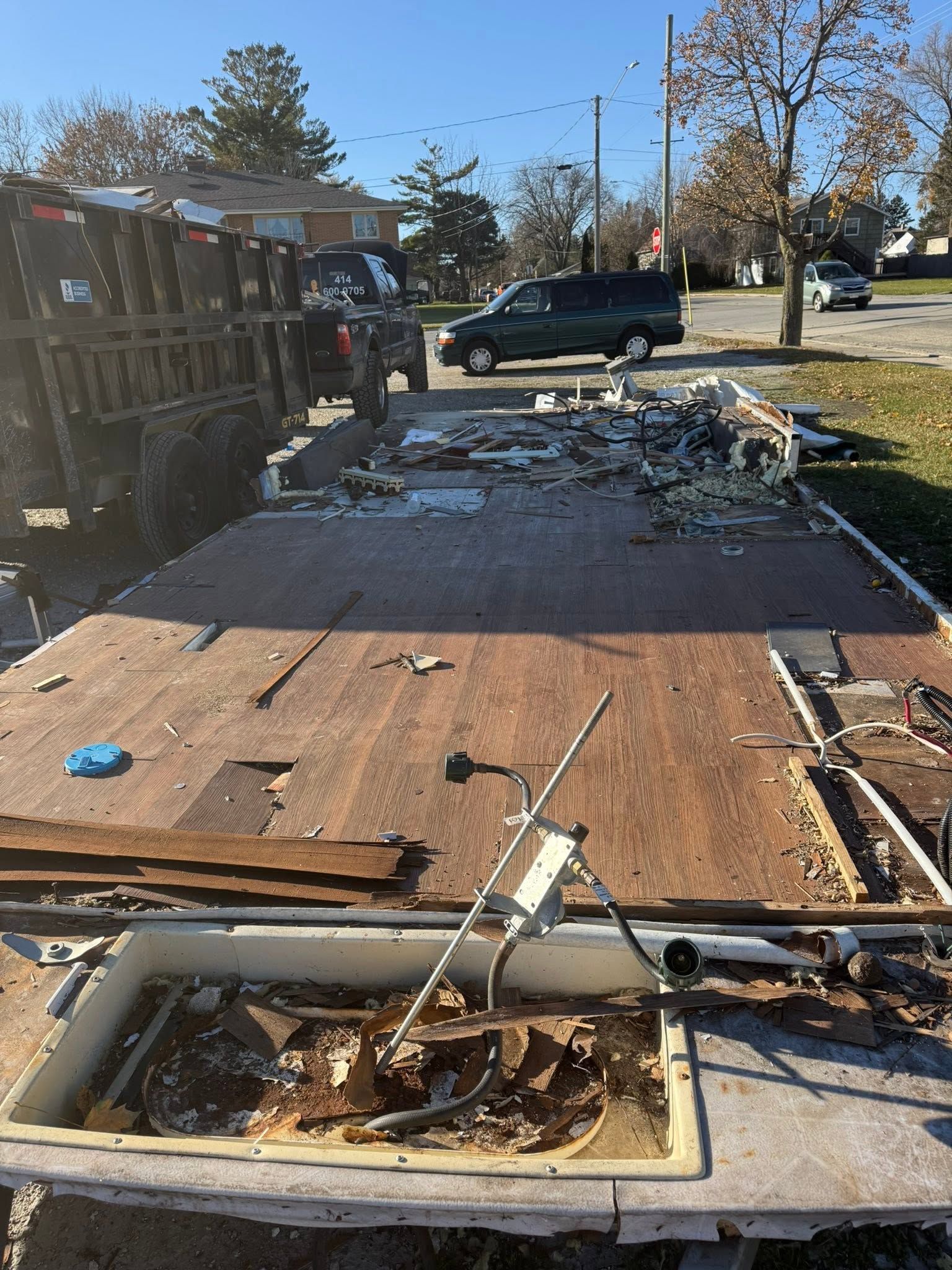 Damaged trailer with debris and broken flooring, parked by a road in daylight