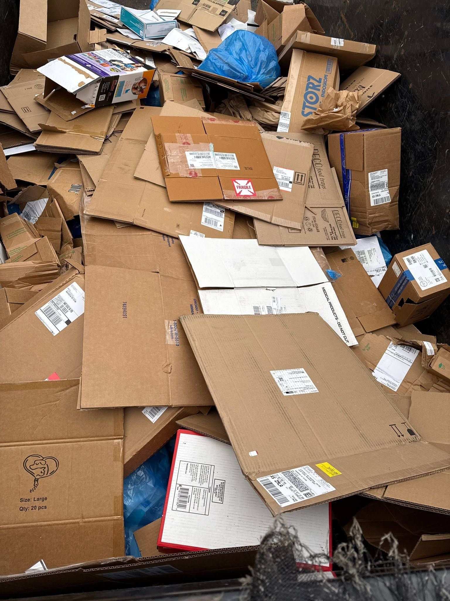 Pile of flattened and broken cardboard boxes, with shipping labels, in a cluttered storage area
