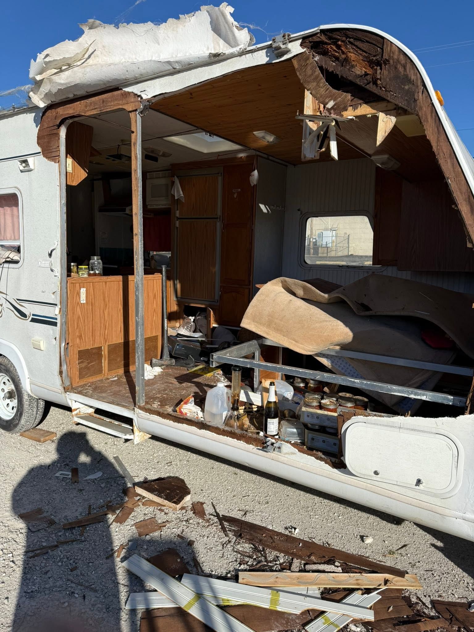 Damaged RV interior exposed after roof collapse, with debris scattered outside.