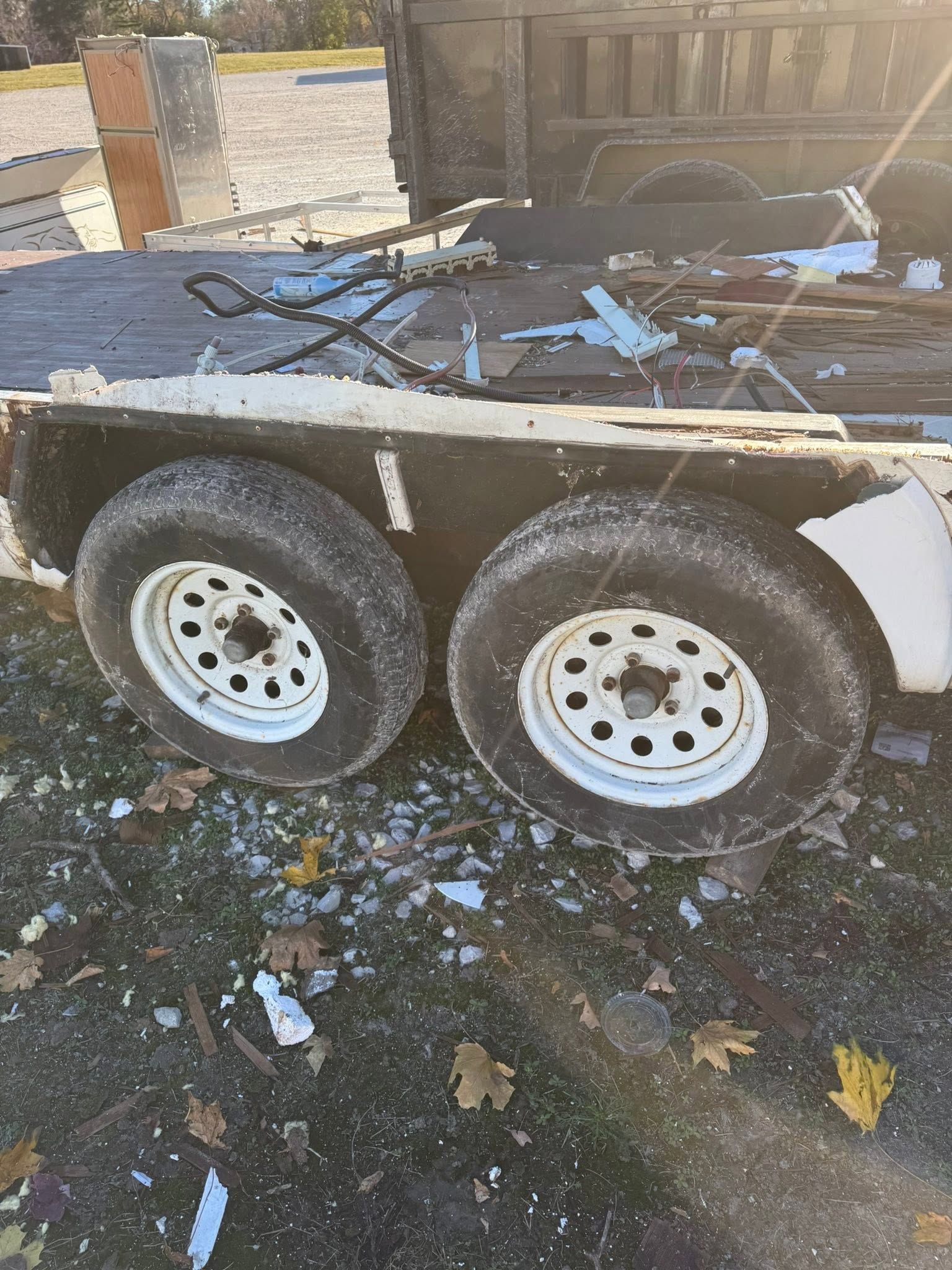 Trailer loaded with debris and scrap metal beside a fence and driveway.