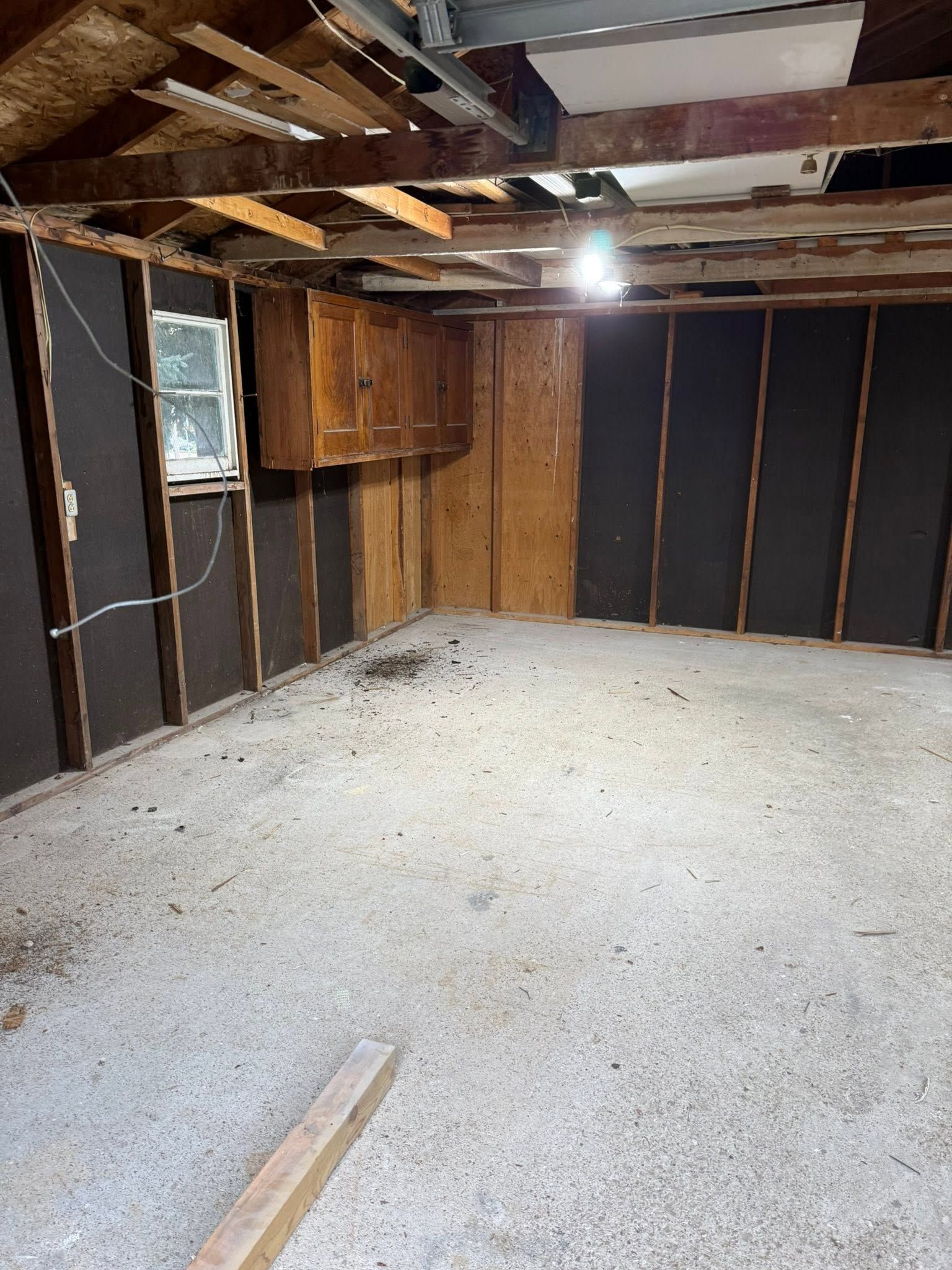 Empty unfinished basement with exposed beams, insulation, and concrete floor under a single light bulb