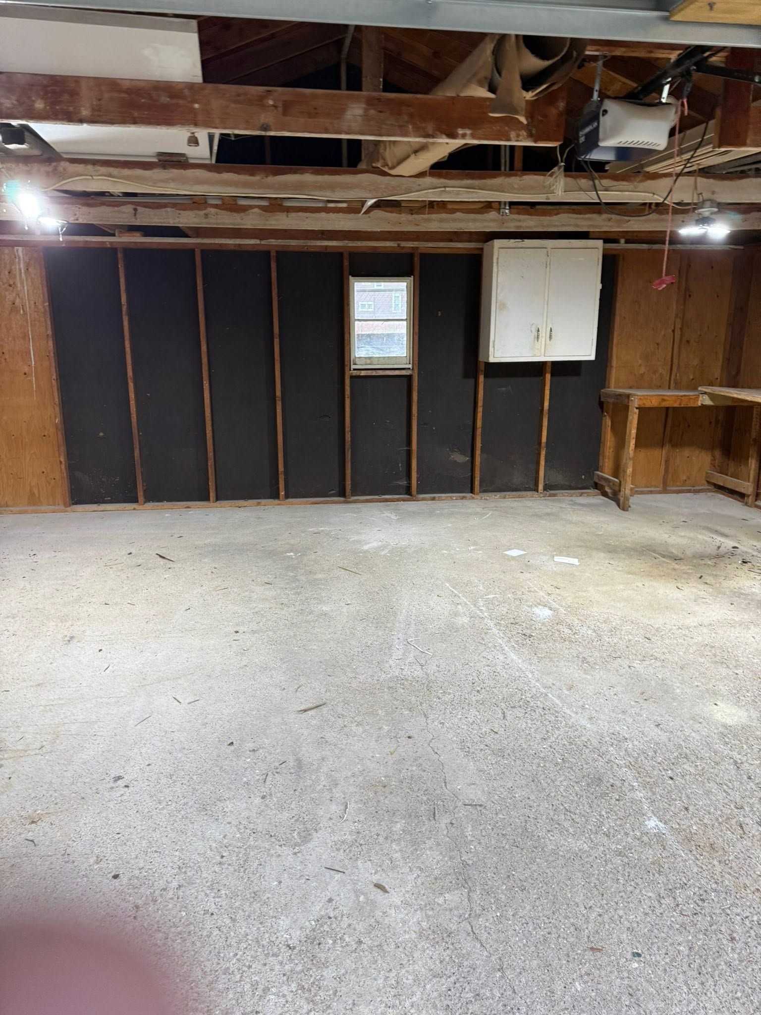 Empty unfinished basement with exposed ceiling, concrete floor, insulated wall, window, and utility panel.