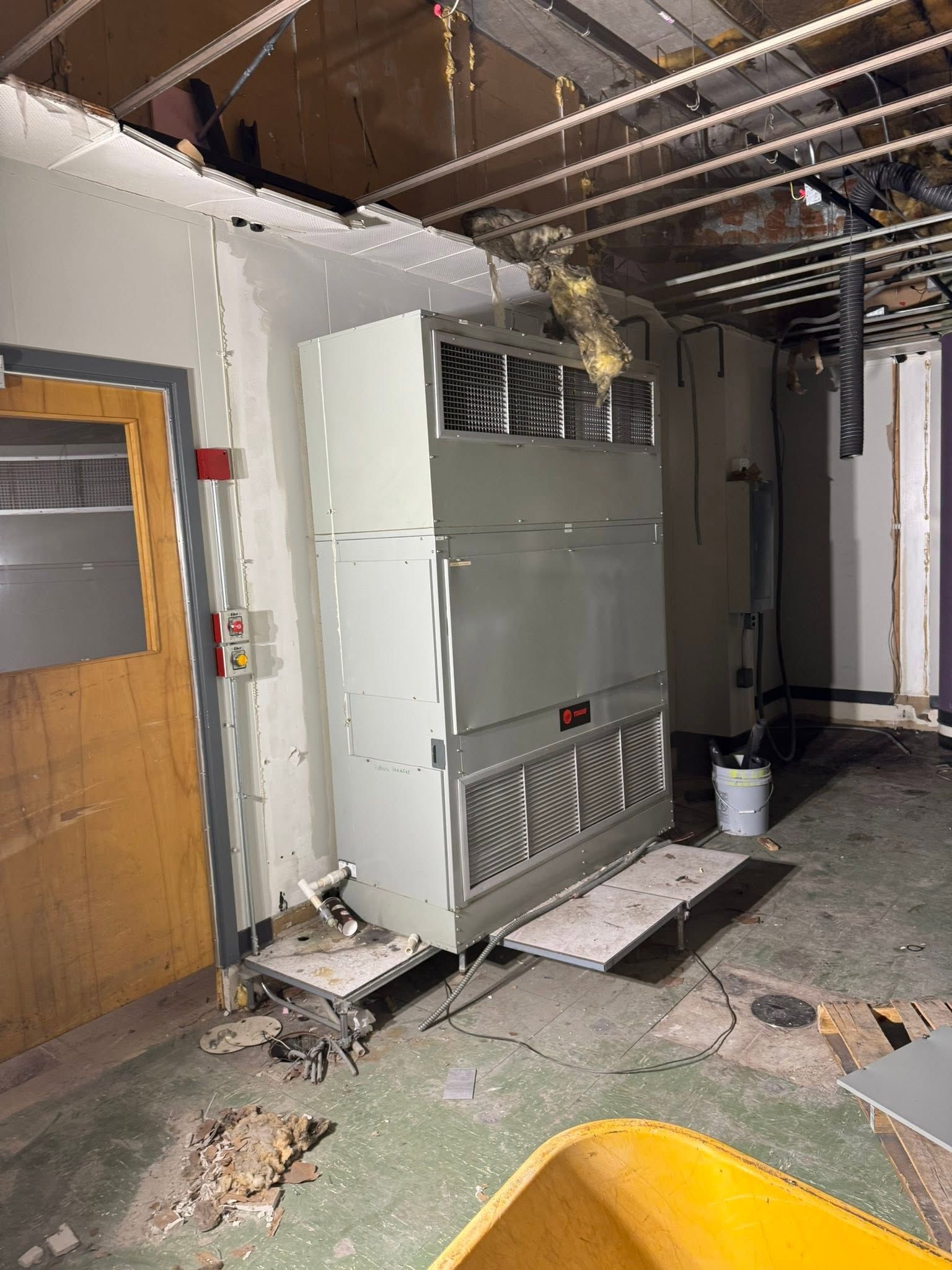 Damaged interior room with exposed ceiling, white cabinet, broken floor, and a wooden door.