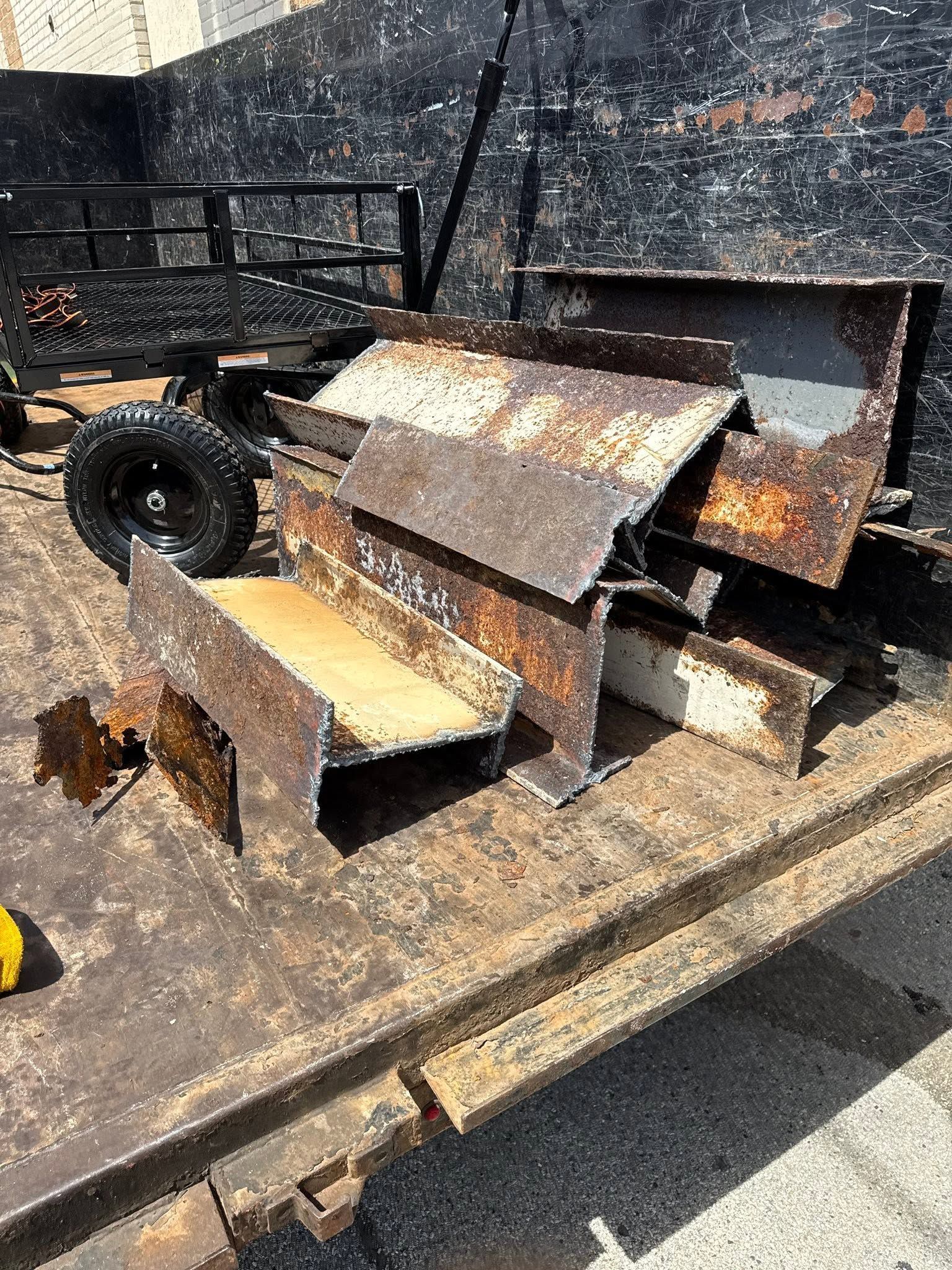 Rusty metal scraps and beams piled on a trailer in an industrial yard