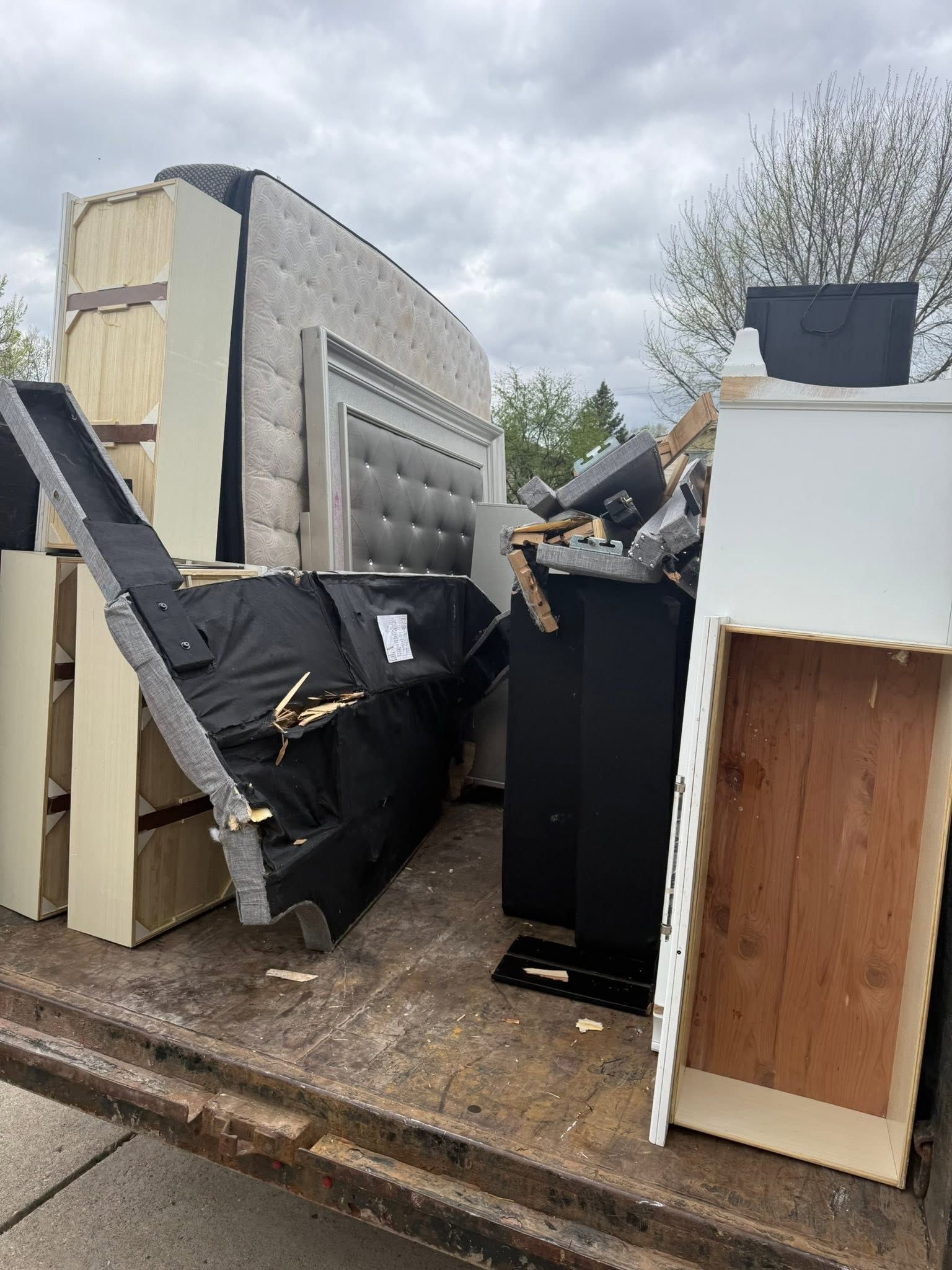 Discarded furniture and mattresses piled on a truck bed in a rainy outdoor dump area.