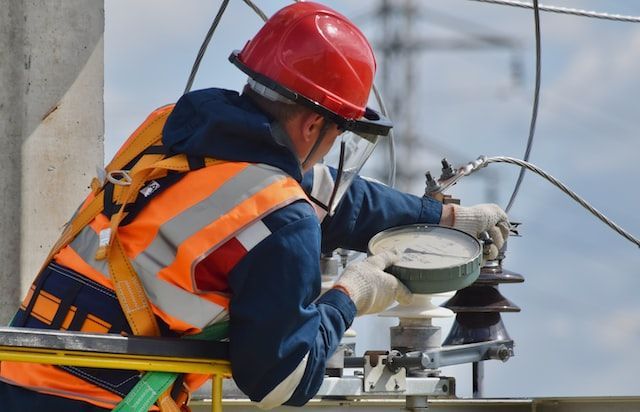 A man wearing a hard hat and safety vest is working on a power line.