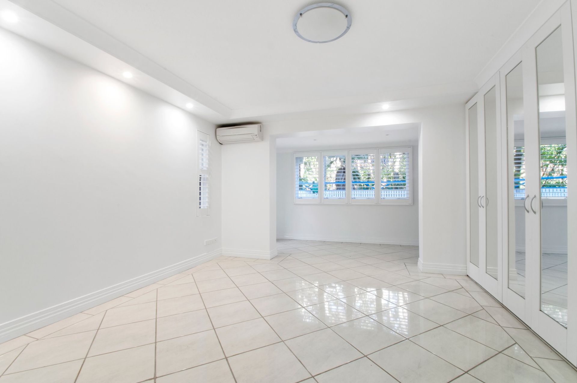 Empty white room with tile floor, large window, built-in closet, and air conditioner.