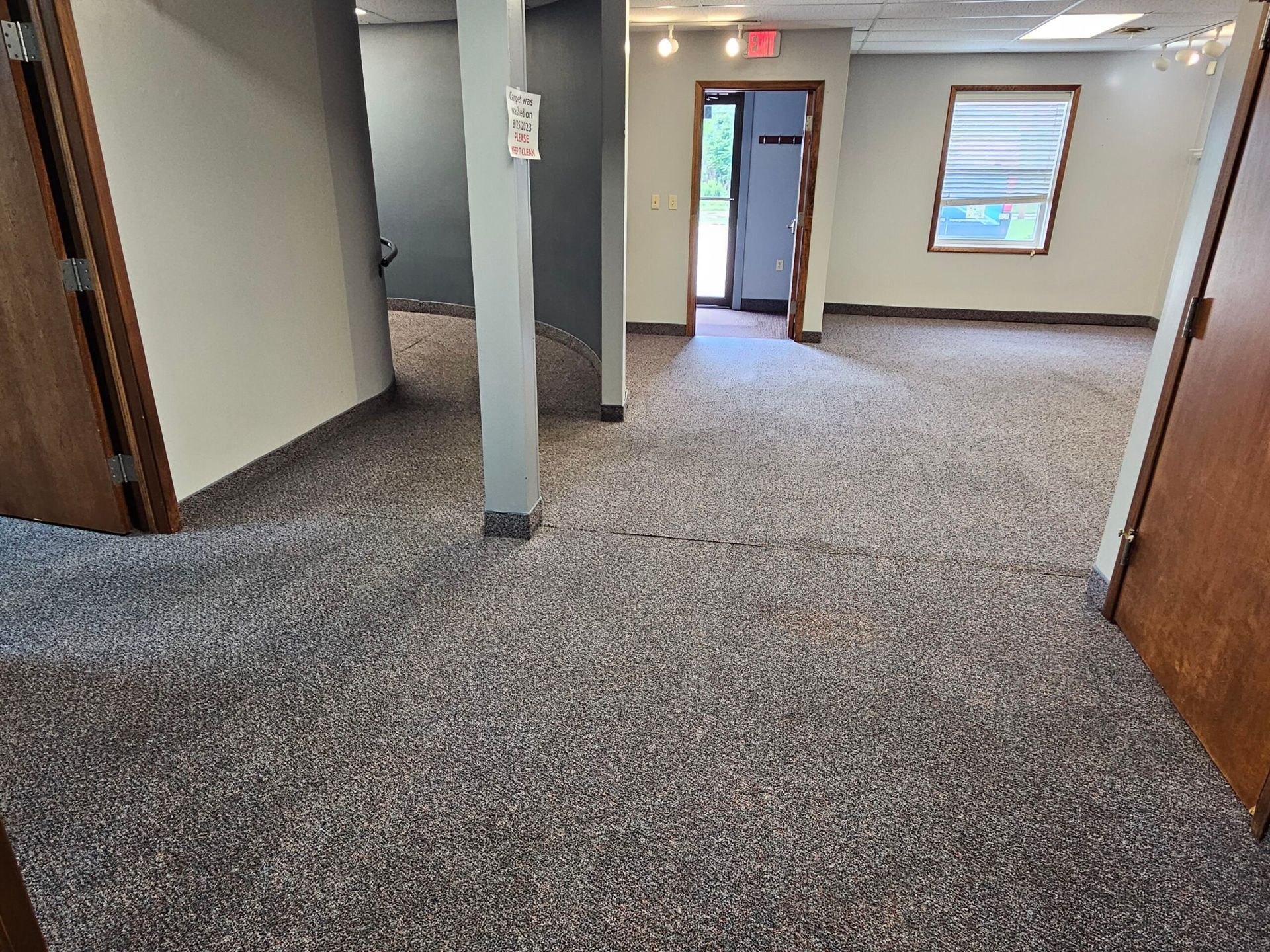 Office interior with gray carpet, beige walls, and brown doors; a hallway with a gray column.