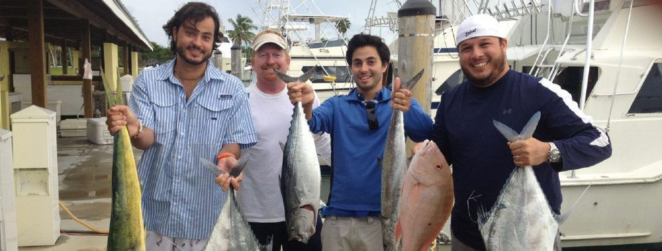 Four people holding up fish, smiling, near a dock with a boat.