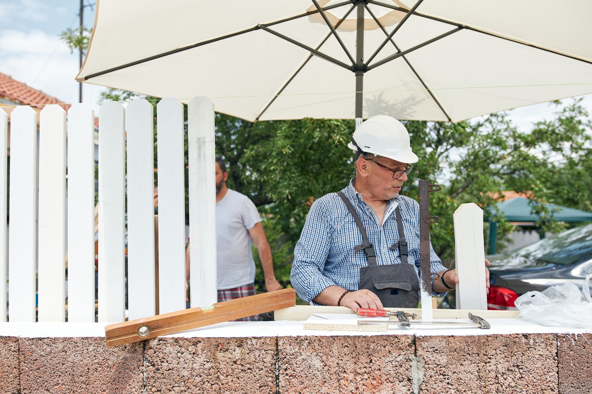 A man working on a white picket fence, demonstrating skills as a new fence installation contractor.