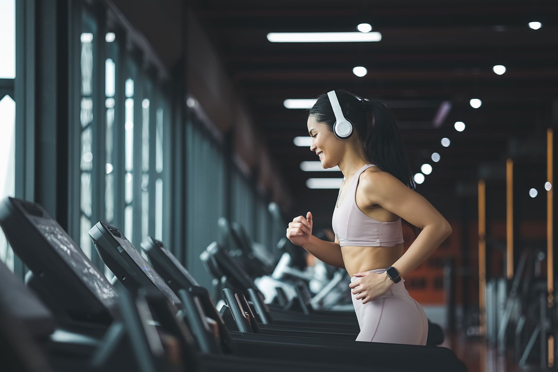 A woman wearing headphones is running on a treadmill in a gym.