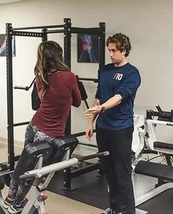 A man is helping a woman do exercises in a gym.