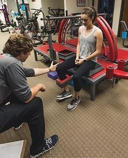 A woman is sitting on a bench in a gym talking to a man.