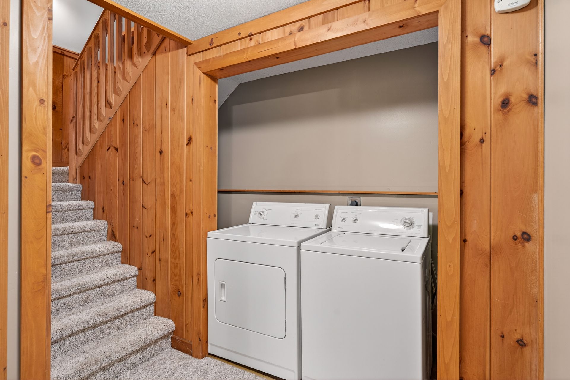 Laundry room with stairs, featuring a washer, dryer, and wood paneling.
