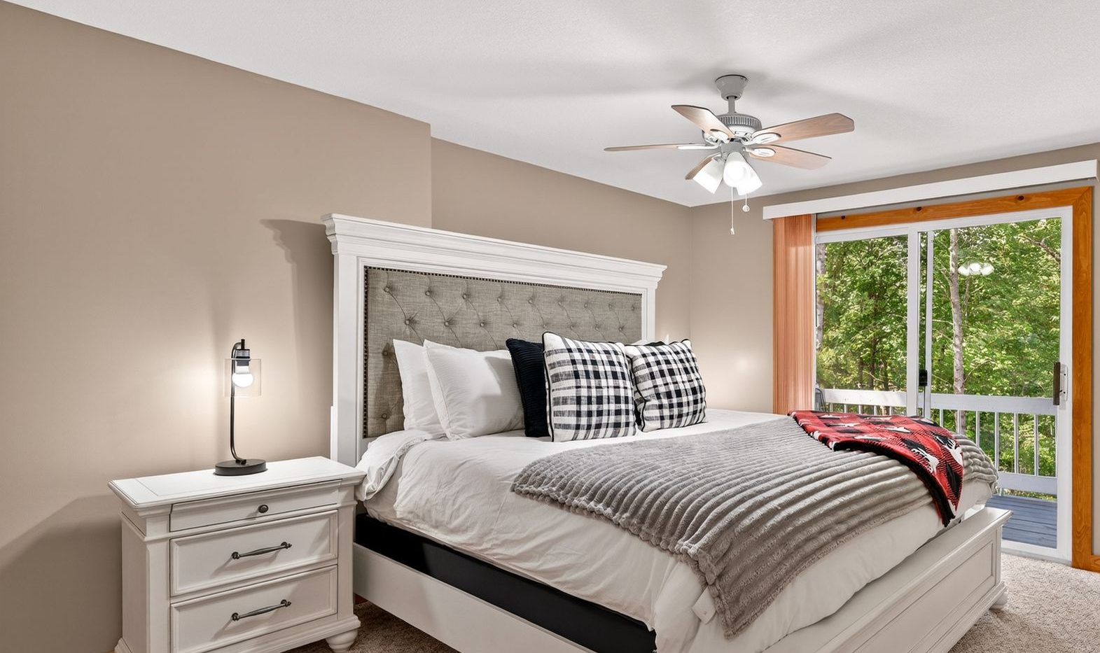 Bedroom with bed, nightstand, sliding door to balcony, and ceiling fan. Beige walls, white bed frame, and natural light.