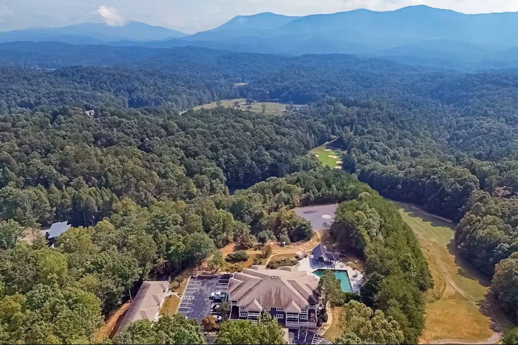 Aerial view of a large house with a pool surrounded by forest and mountains in the distance.
