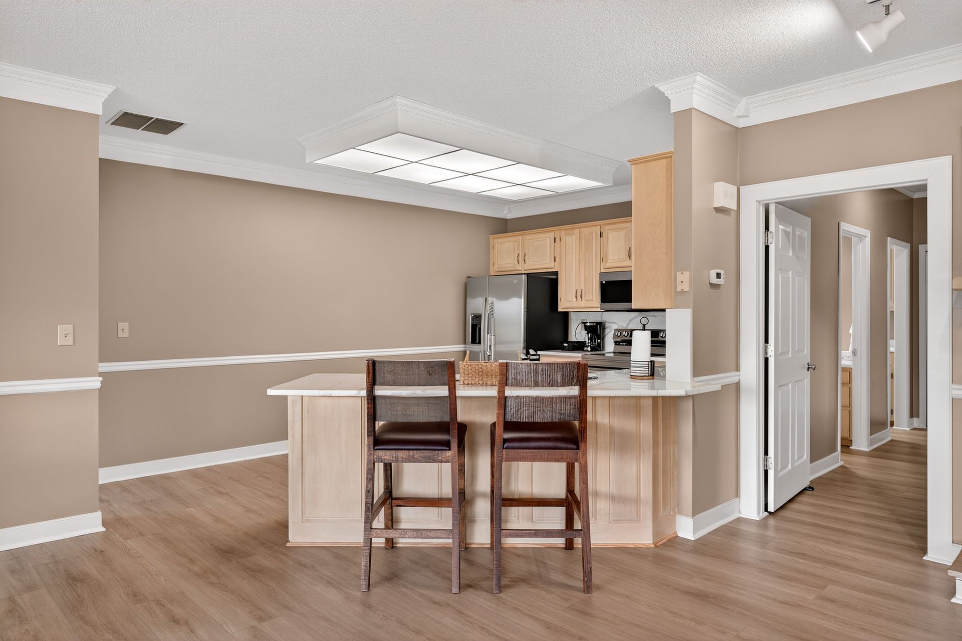 Open kitchen with bar stools, beige walls, wood floor, and entryways.