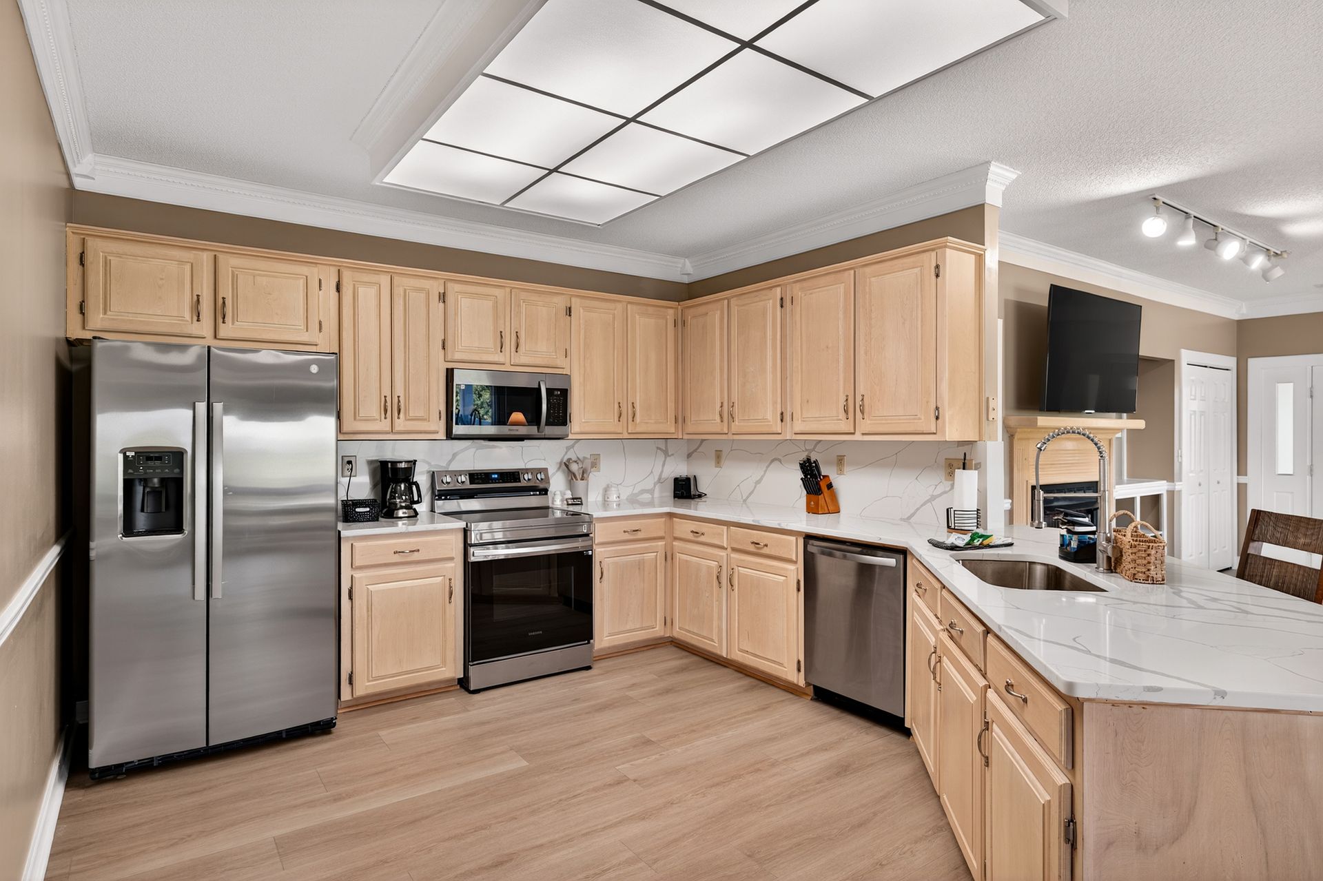 A kitchen with light wood cabinets, stainless steel appliances, and a white countertop.