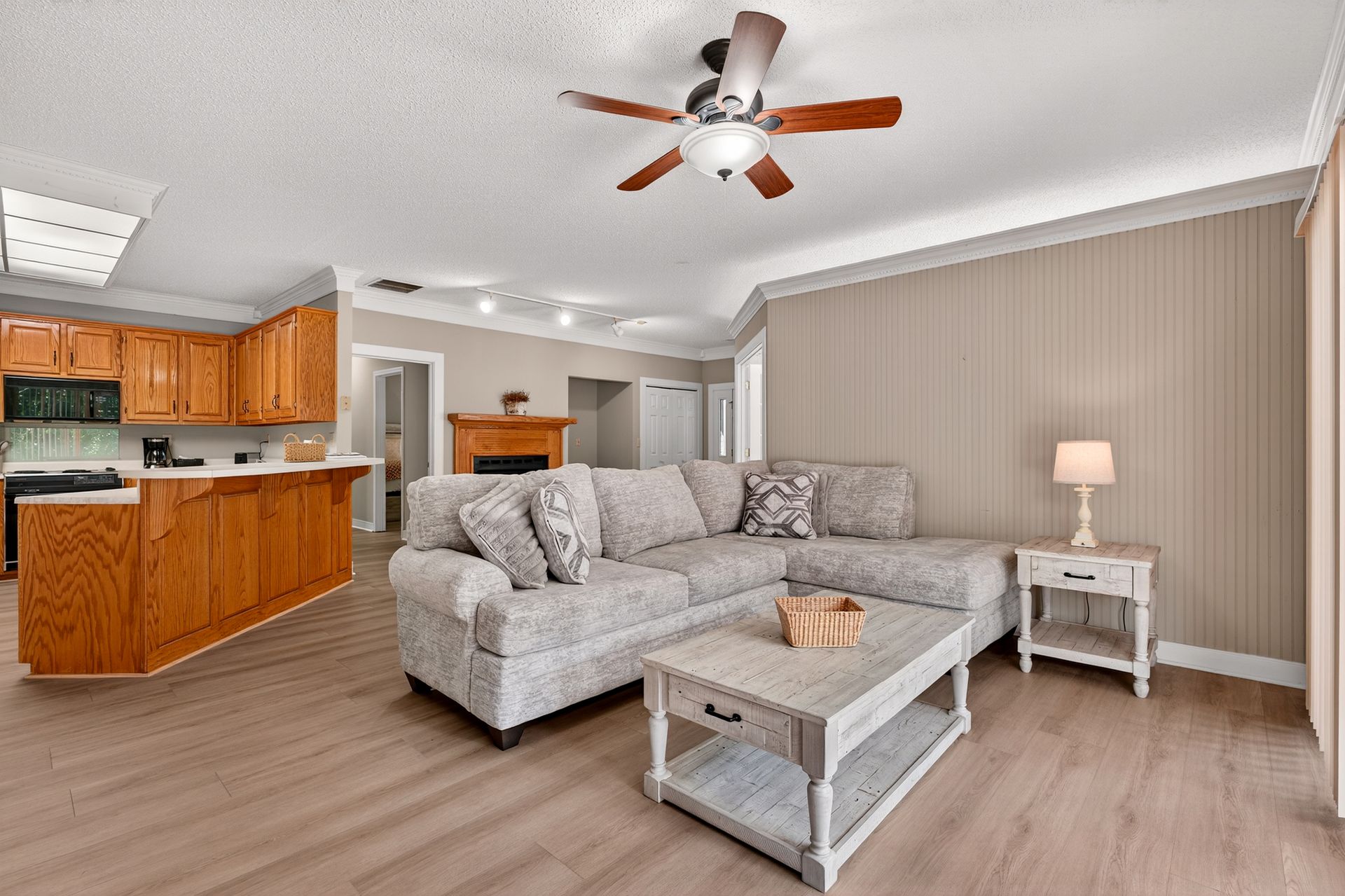Living room with light wood floors, a gray sectional, and a wooden kitchen.