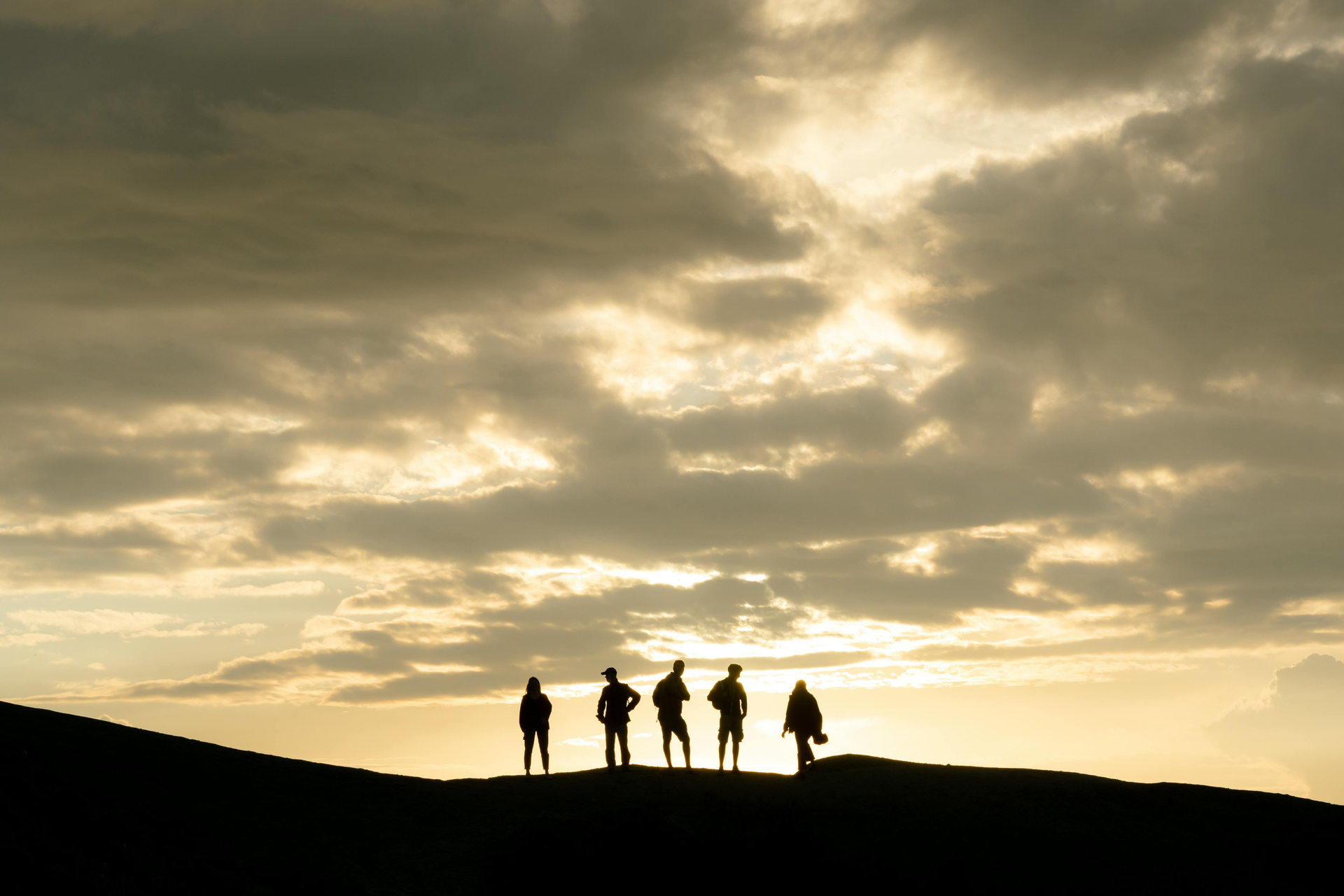 Silhouetted figures on a hilltop against a cloudy, golden sky at sunset.