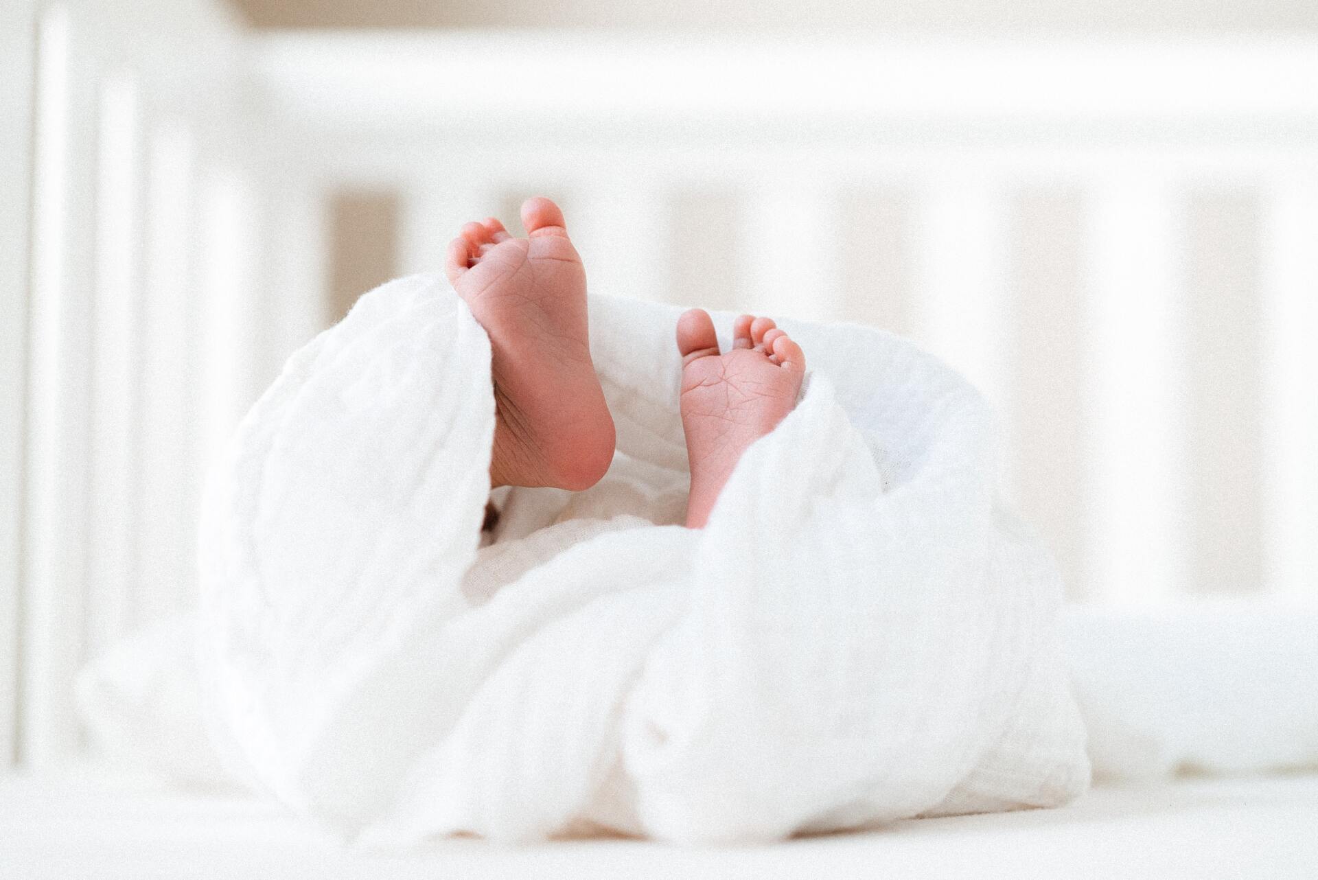 Little baby feet with ten tiny toes in a white crib with a linen blanket
