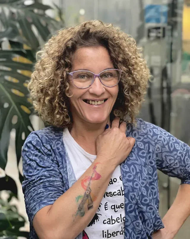 Uma mulher de cabelos cacheados usando óculos e uma tatuagem no braço