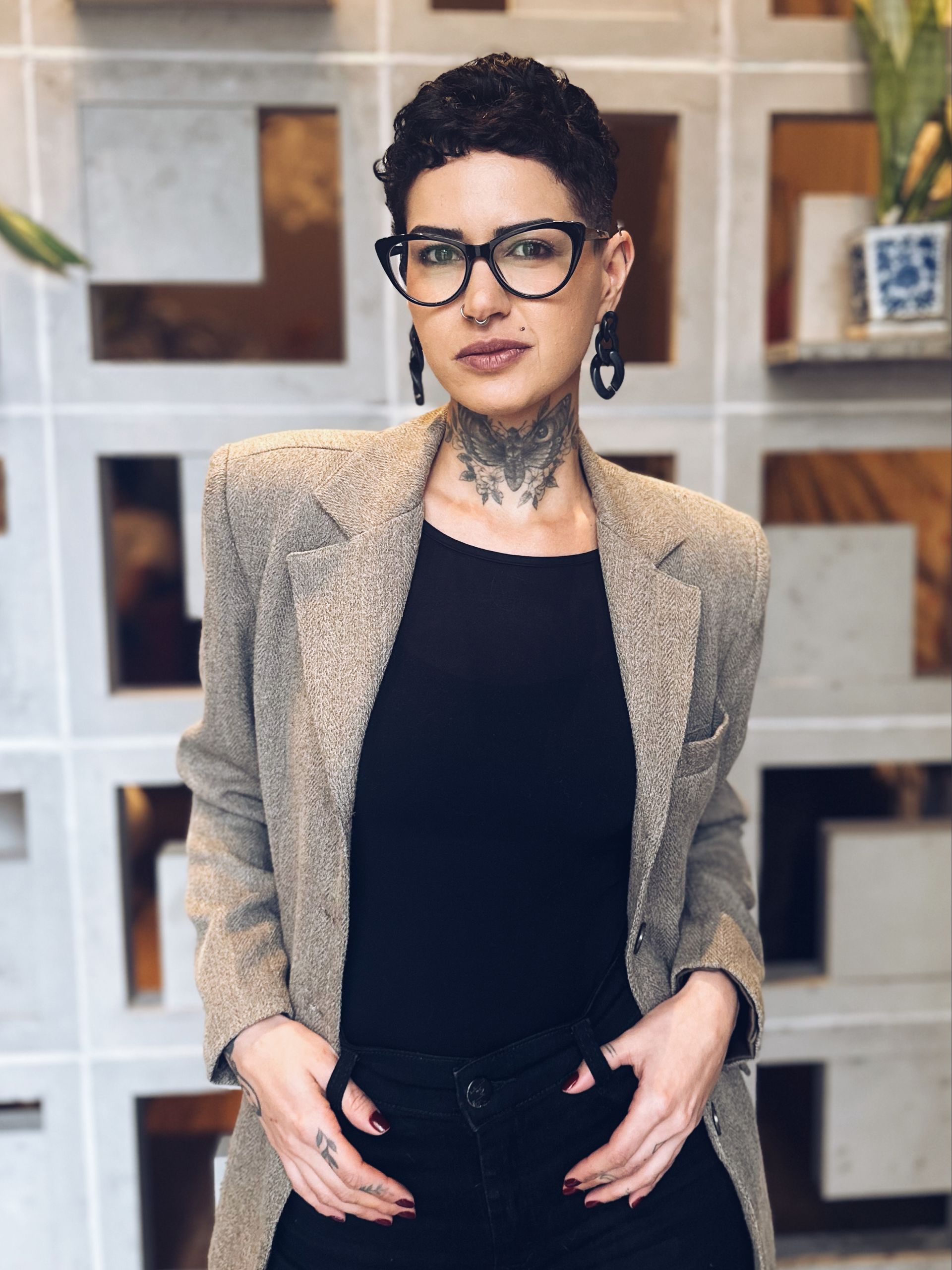 Uma mulher usando óculos e uma camisa preta está parada em frente a uma parede.