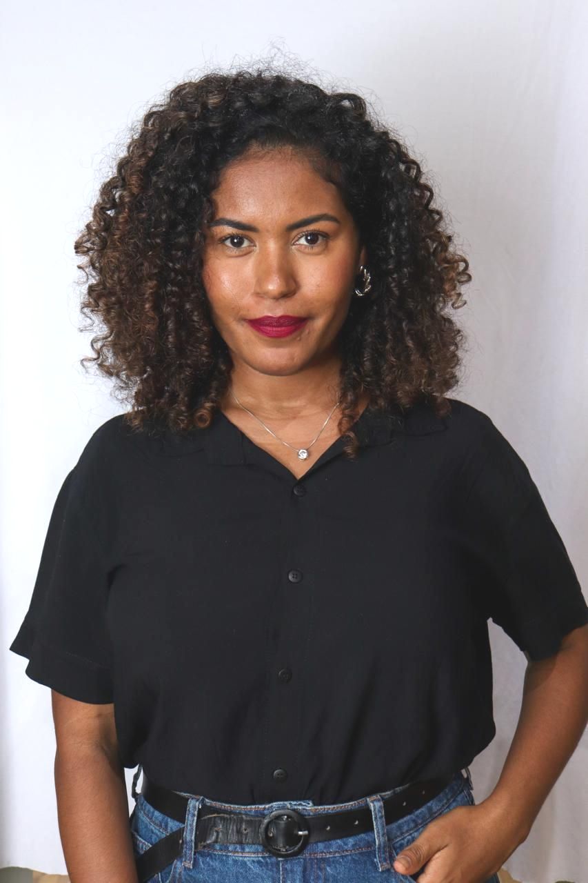 Uma mulher com cabelos cacheados está vestindo uma camisa preta e jeans.
